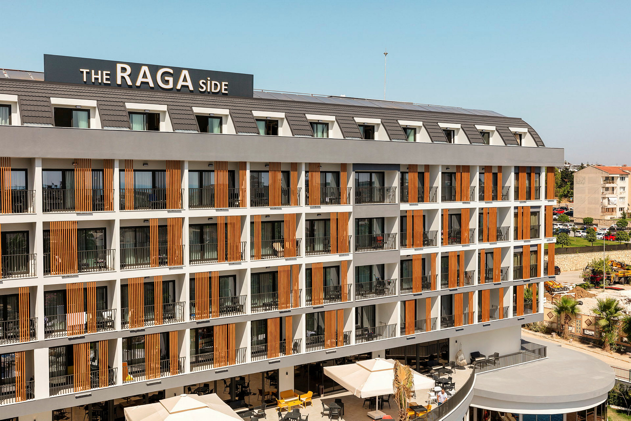 Hotelkompleks med flere etager med altaner og et skilt, der viser navnet 'The RAGA Side'. (AI-genereret tekst)