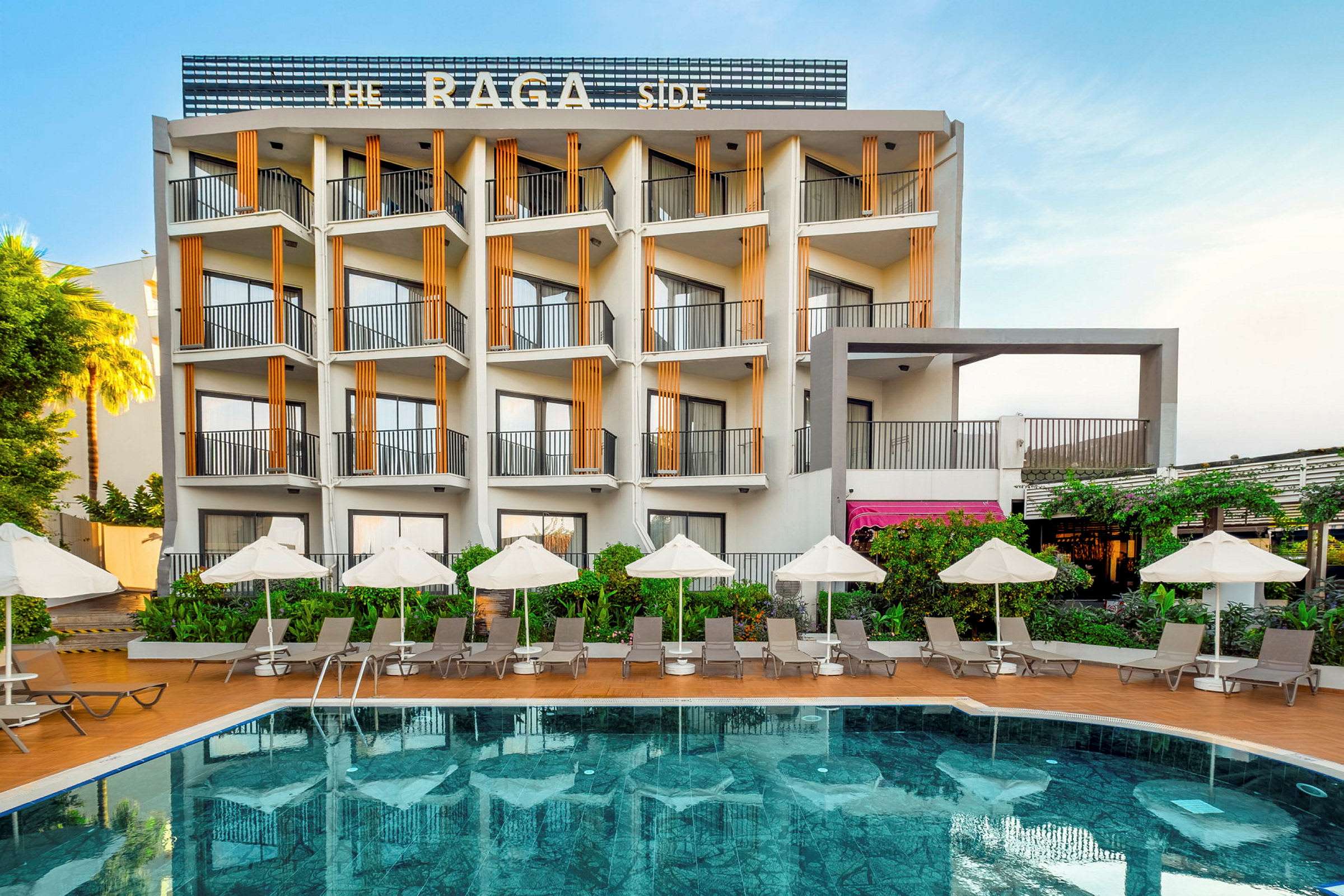 Et hotel bygget i moderne linjer med en udendørs pool foran, omgivet af liggestole og parasoller. (AI-genereret tekst)