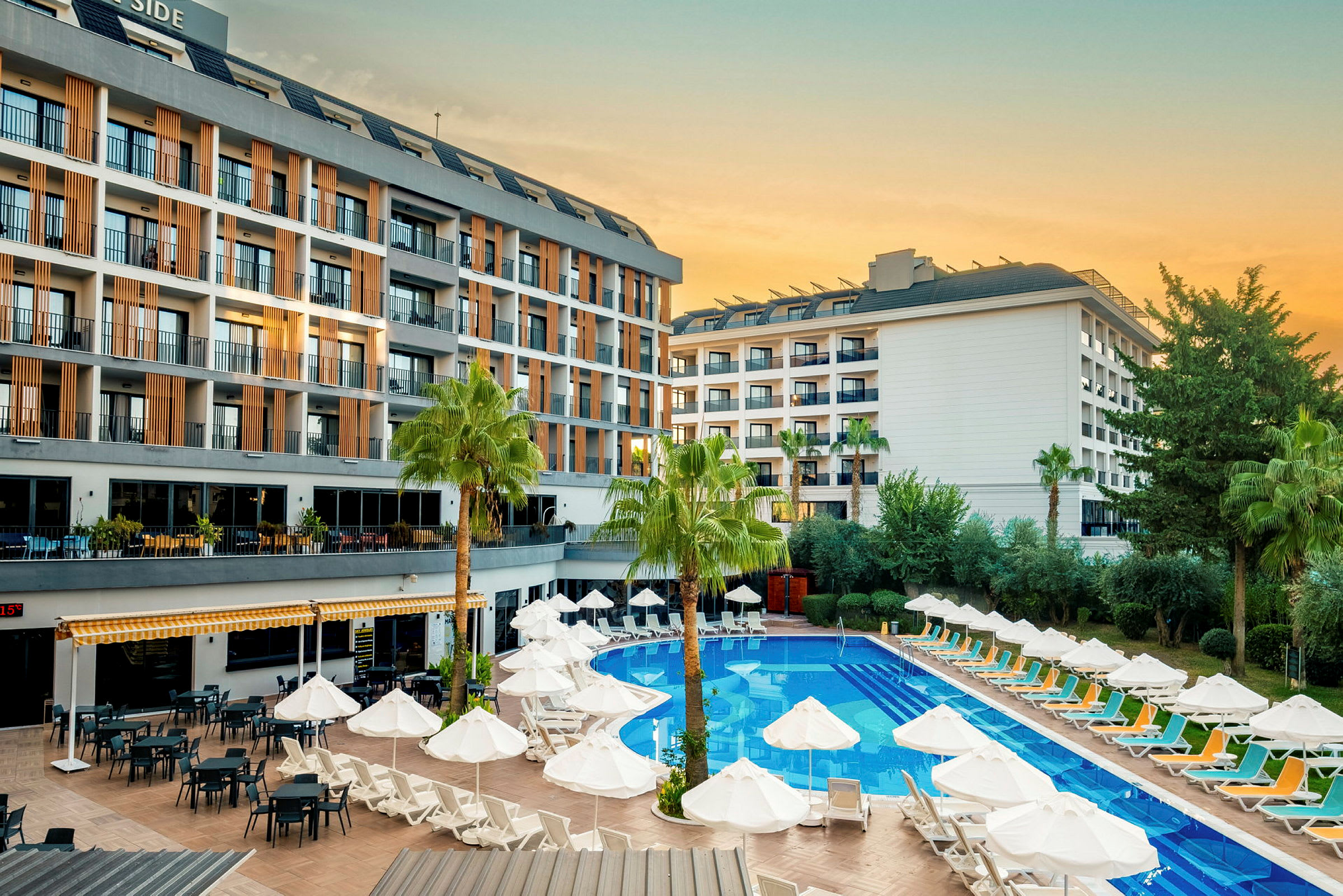Hotelbygning med poolområde, liggestole og parasoller. (AI-genereret tekst)