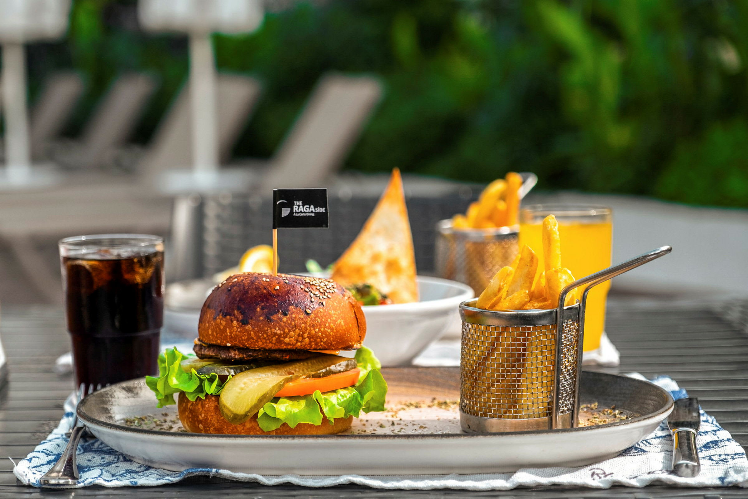 En tallerken med en burger, pommes frites og en drik udendørs. (AI-genereret tekst)