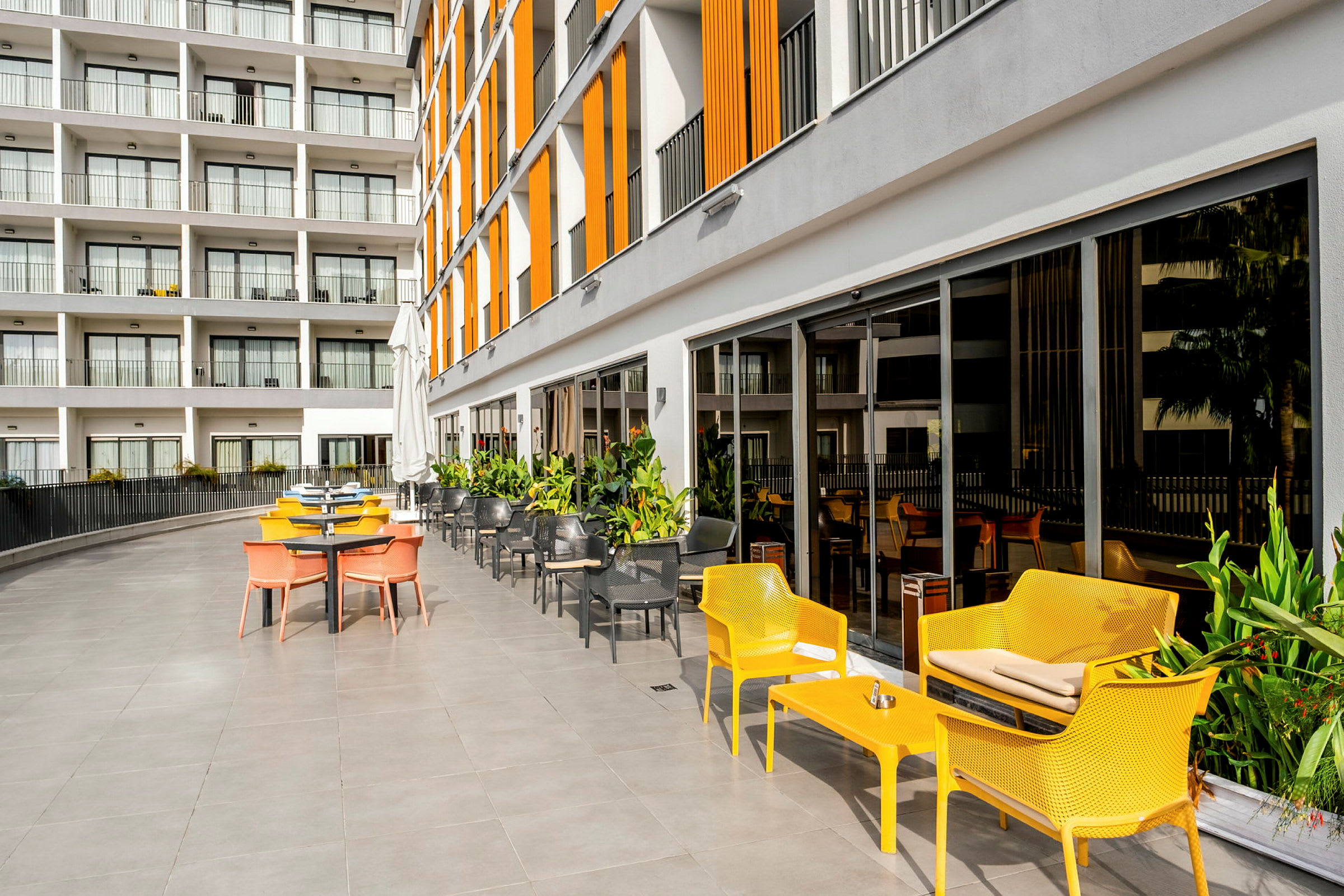 Udendørs serveringsområde med farverige stole og et moderne hotel i baggrunden. (AI-genereret tekst)