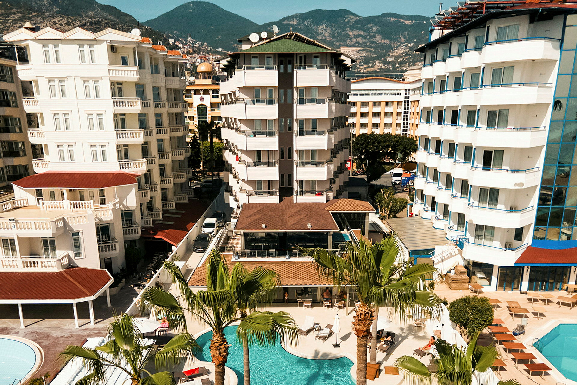 Udsigt over et hotelområde med flere bygninger, altaner og en swimmingpool omgivet af palmer. (AI-genereret tekst)