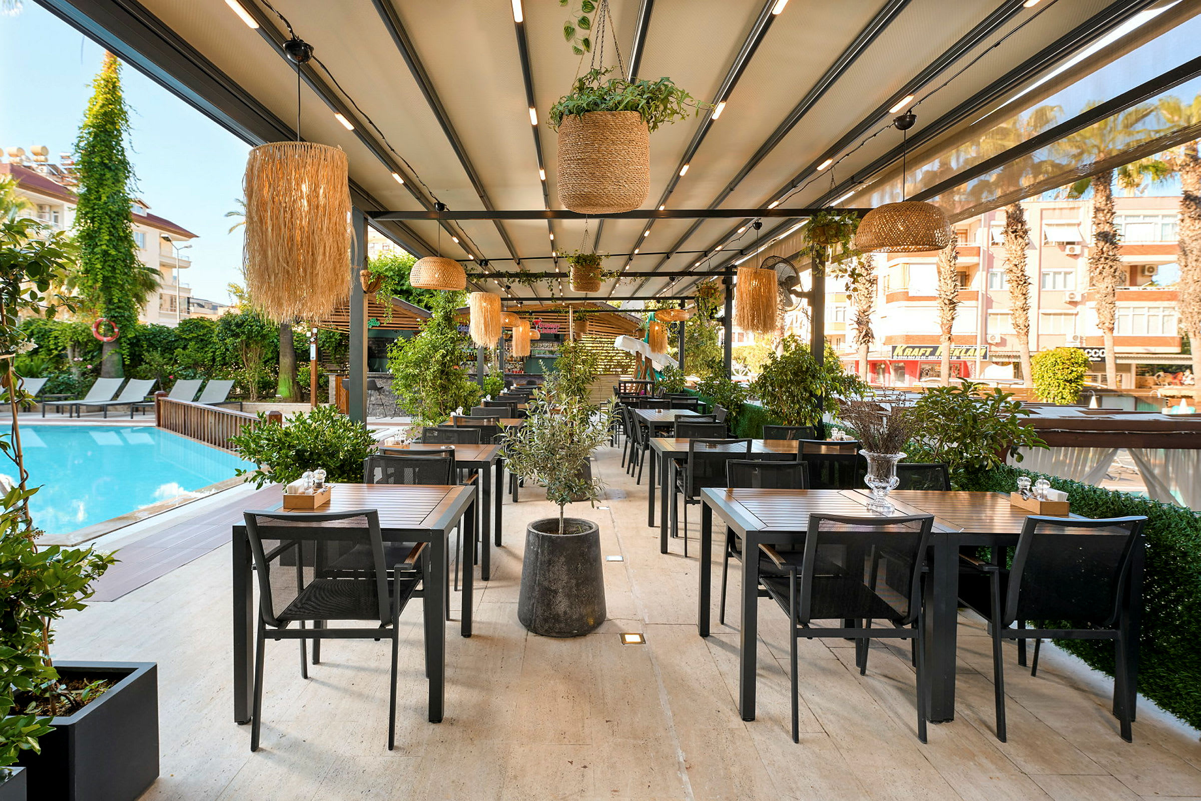 Udendørsrestaurant ved en pool med borde og stole samt grønne planter. (AI-genereret tekst)