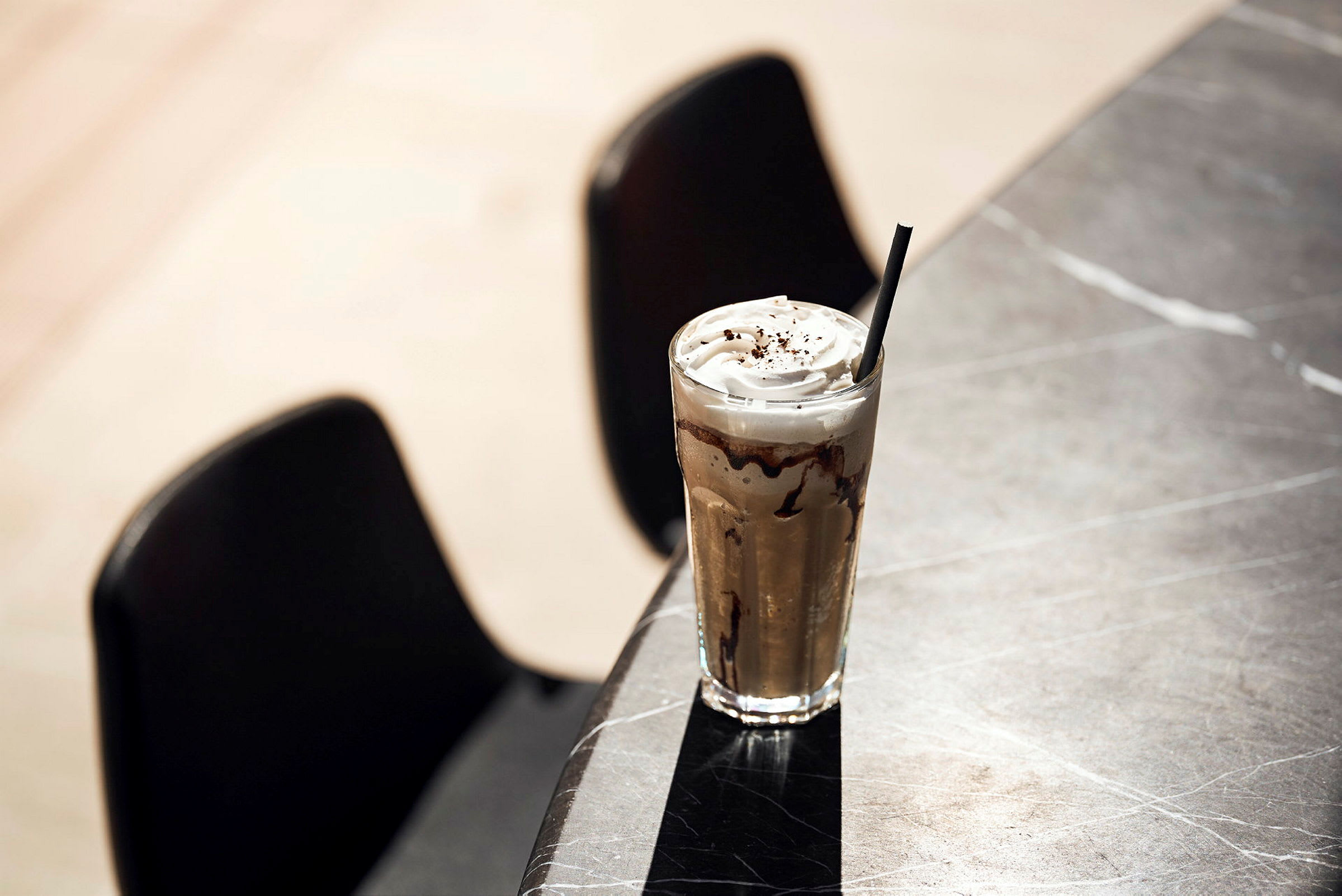 Et glas iskaffe med flødeskum og chokolade dekorerer et bord. (AI-genereret tekst)