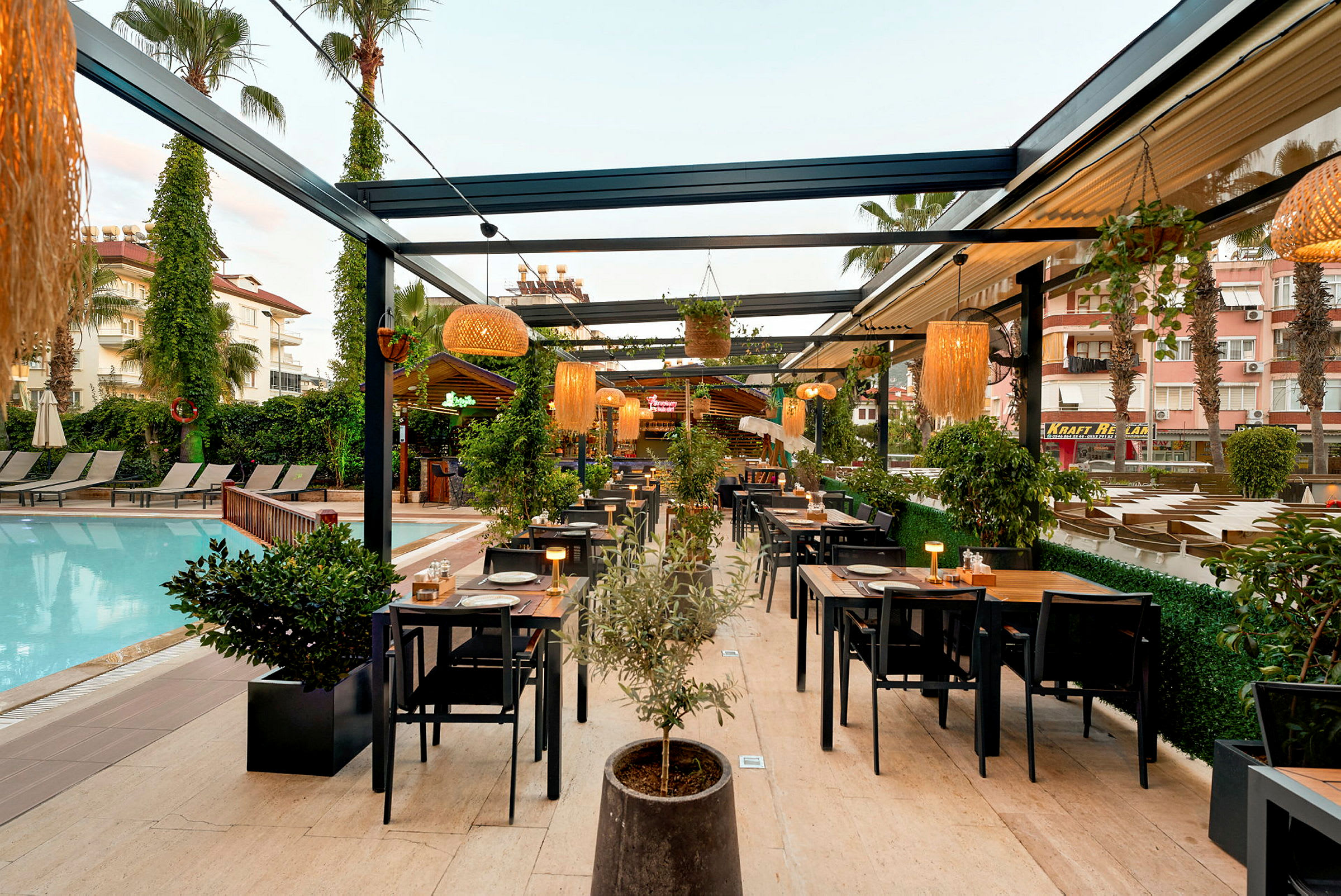 Udendørsrestaurant ved en pool med borde og stole samt planter og belysning. (AI-genereret tekst)