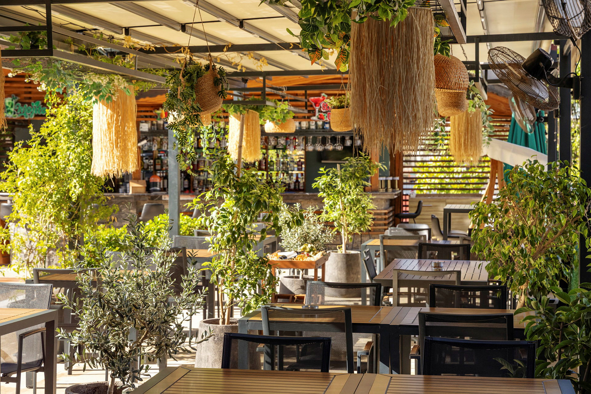 En udendørs restaurant dækket af planter og dekorationer med træborde og stole. (AI-genereret tekst)