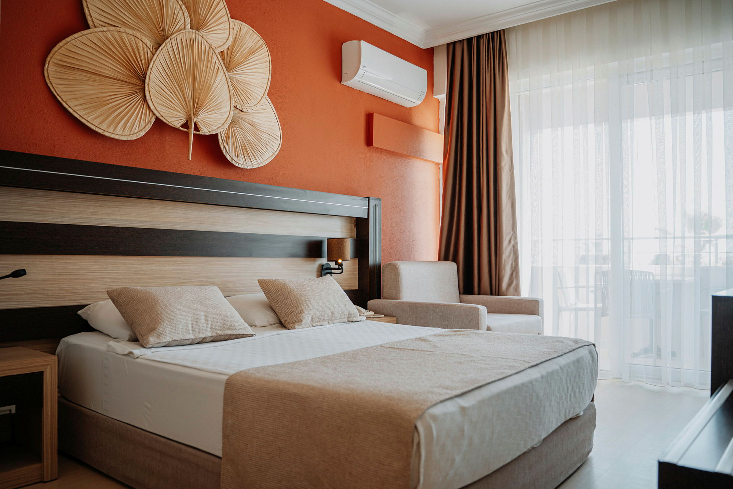 Hotelværelse med orange væg, dobbeltseng med to puder og dekorative genstande over sengen. (AI-genereret tekst)
