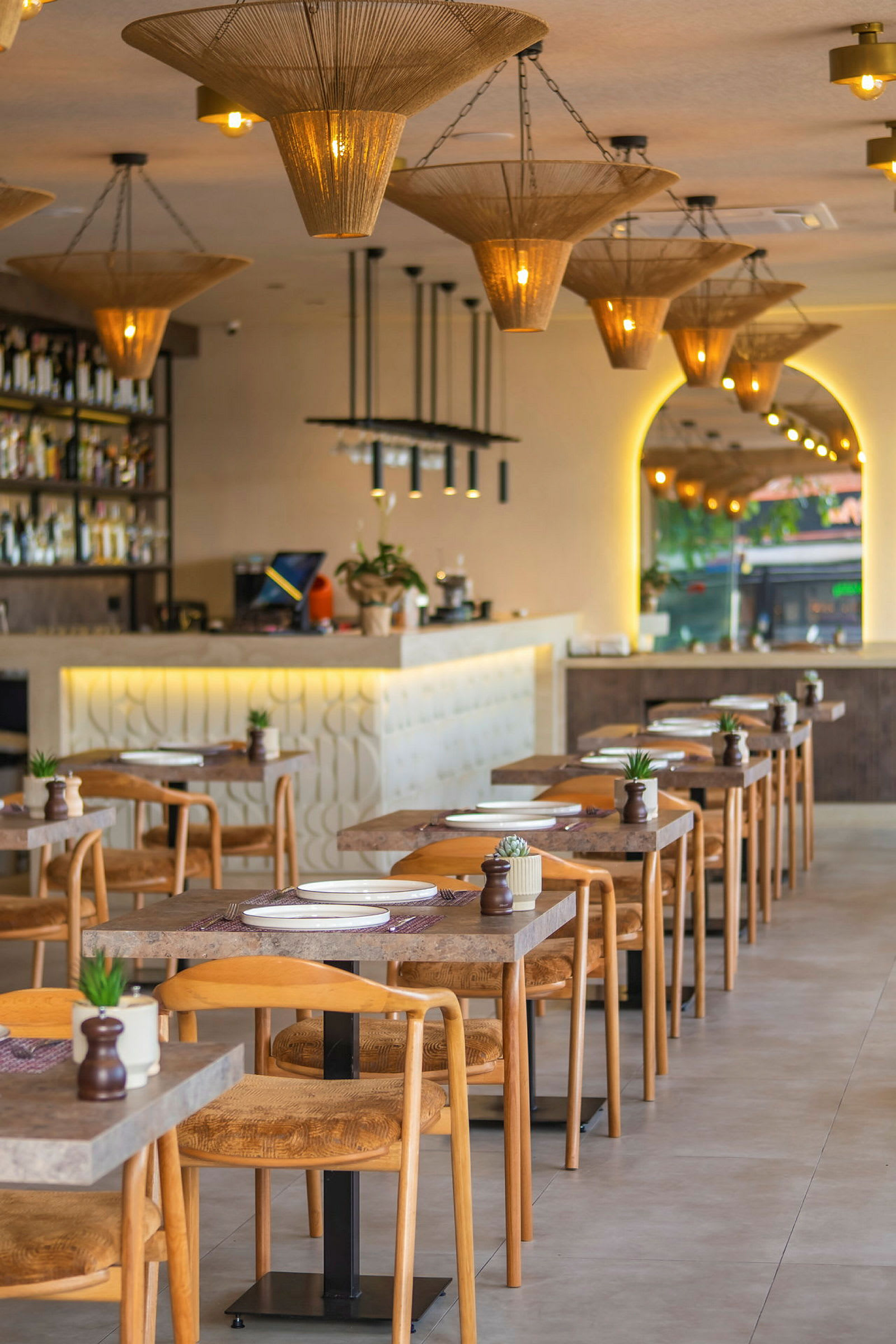 Billede af en moderne restaurant med opsatte borde og stole, samt dekorative loftslamper. (AI-genereret tekst)