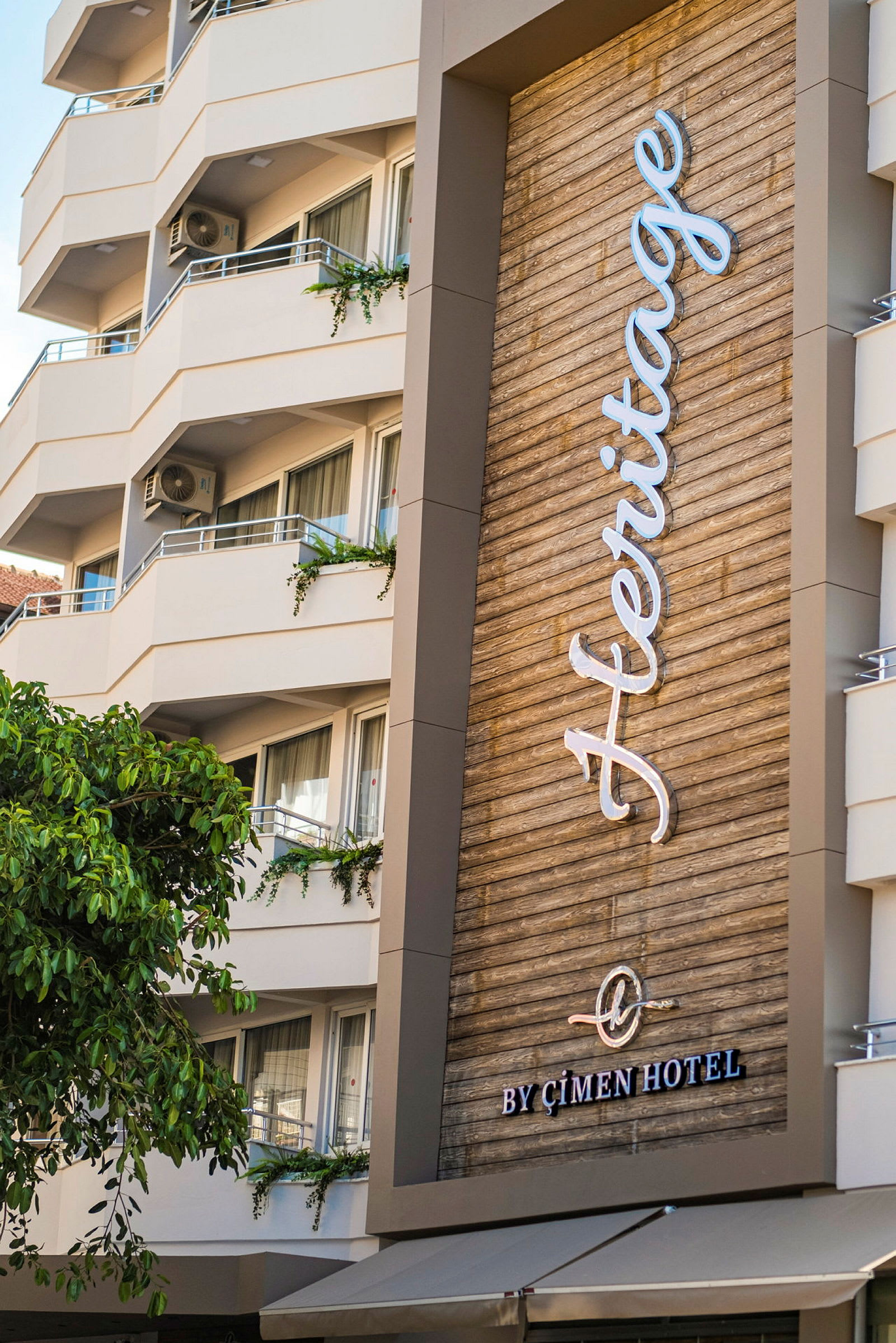 Et moderne hotel med altaner og et skilt med teksten 'Heritage by Çimen Hotel'. (AI-genereret tekst)