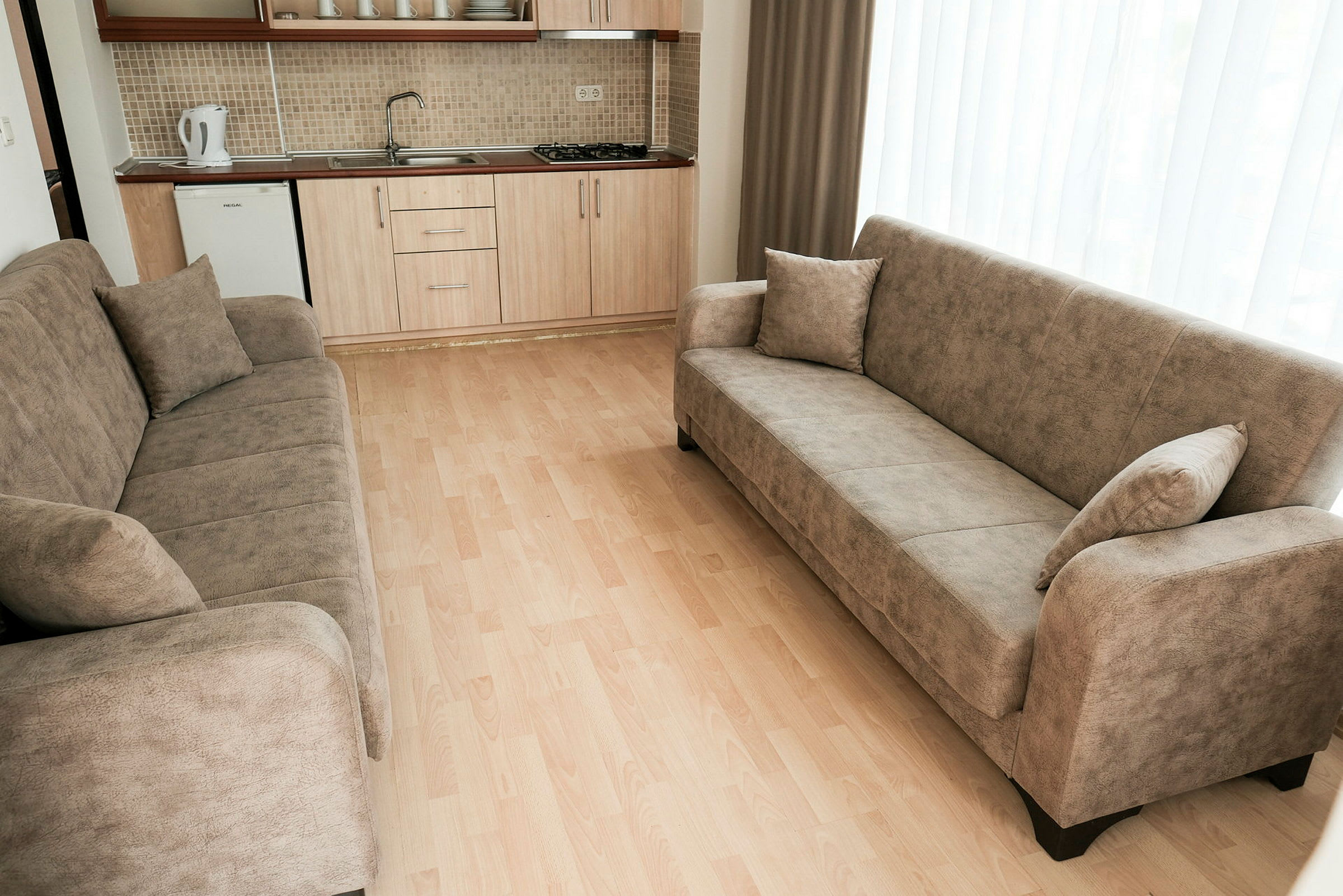 En stue med to beige sofaer og et køkken i baggrunden. (AI-genereret tekst)