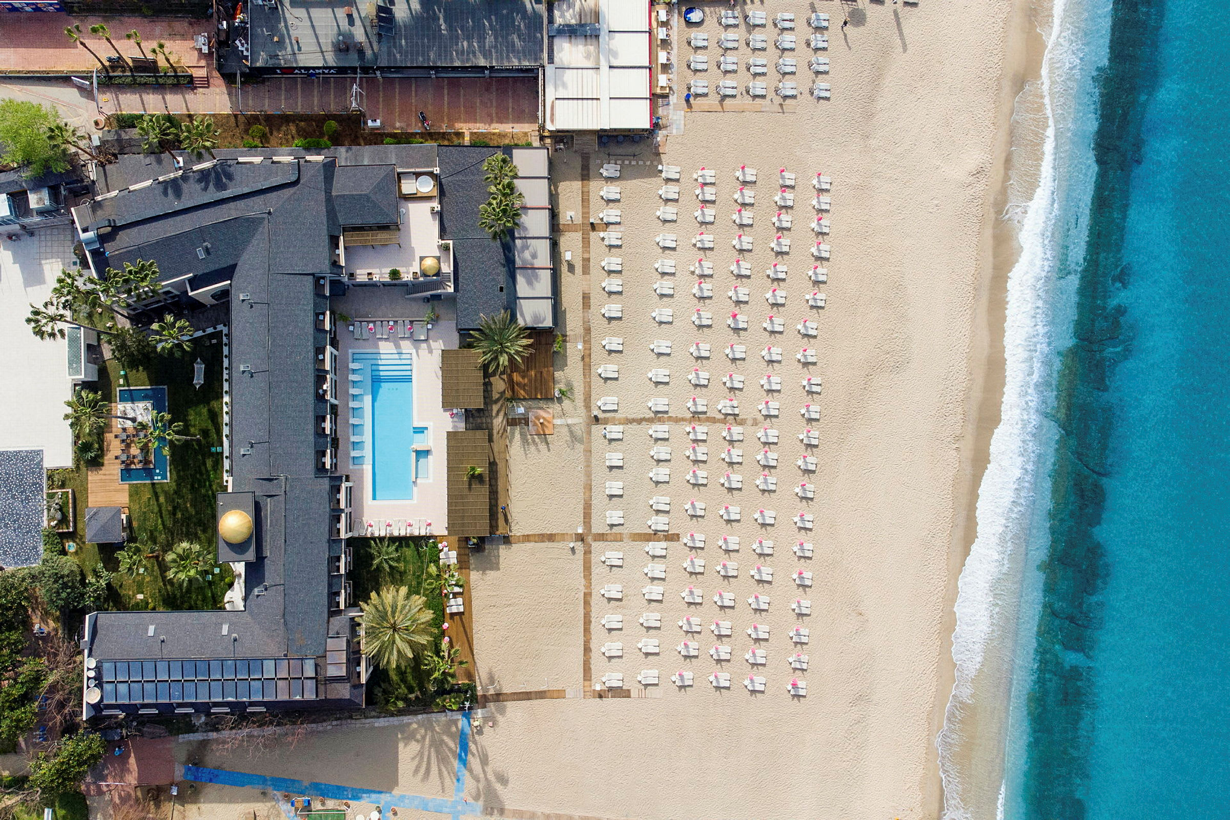 Luftfoto af en strand med solsenge, et hotelområde med pool og havet. (AI-genereret tekst)