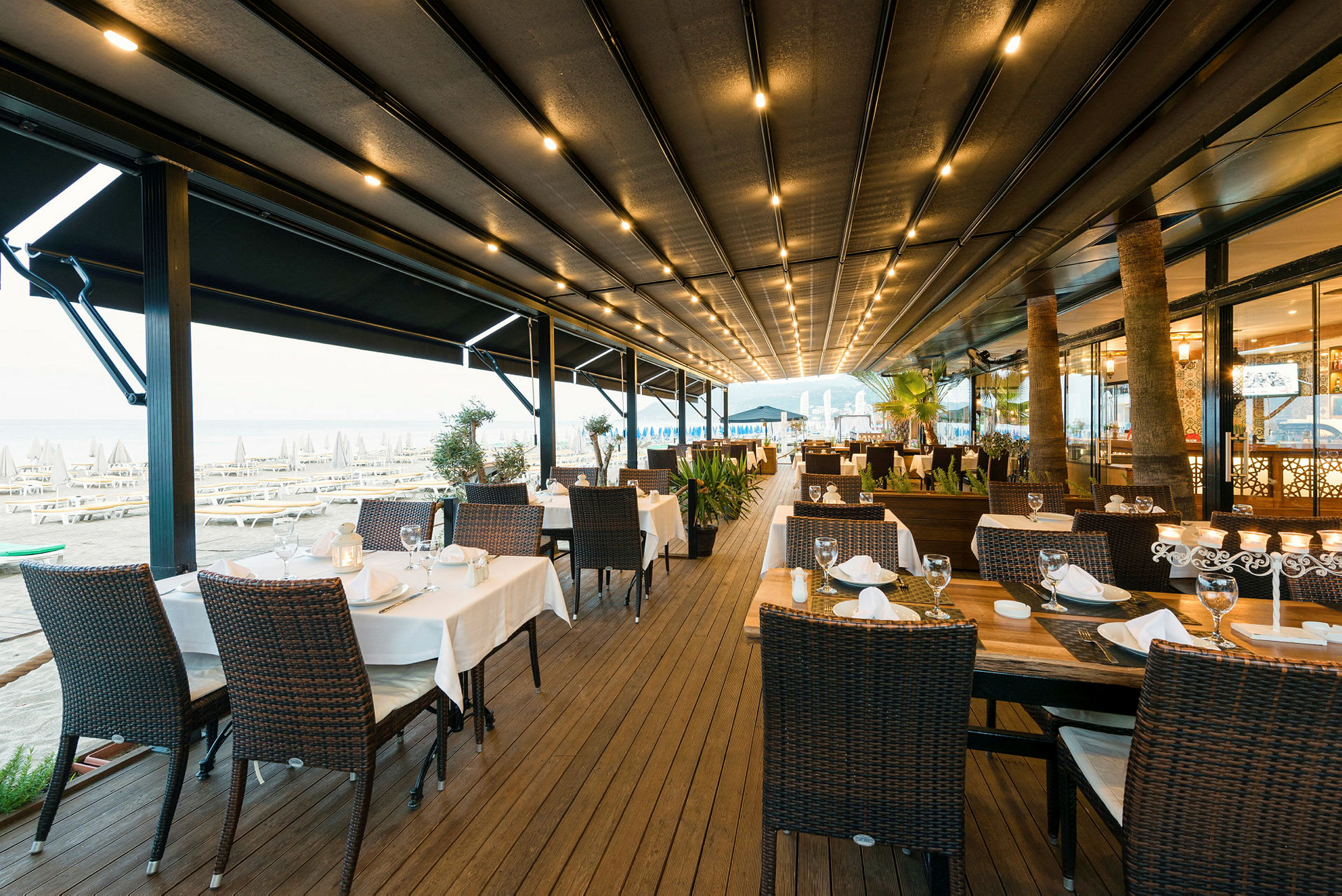 En udendørs restaurant med dækkede borde og stole tæt på stranden. (AI-genereret tekst)