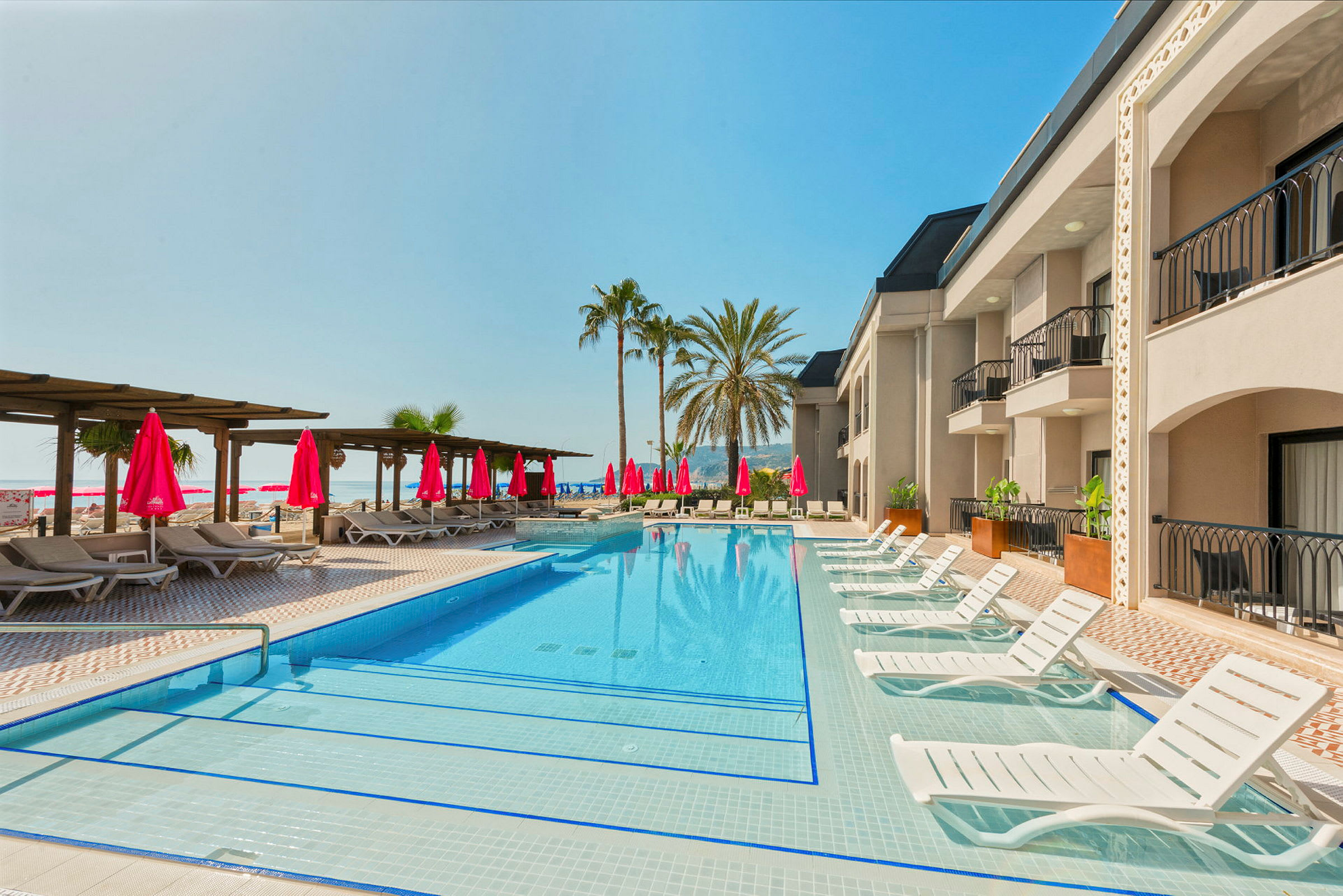 Udendørs swimmingpool ved et hotel, omgivet af liggestole og parasoller med palmer i baggrunden. (AI-genereret tekst)