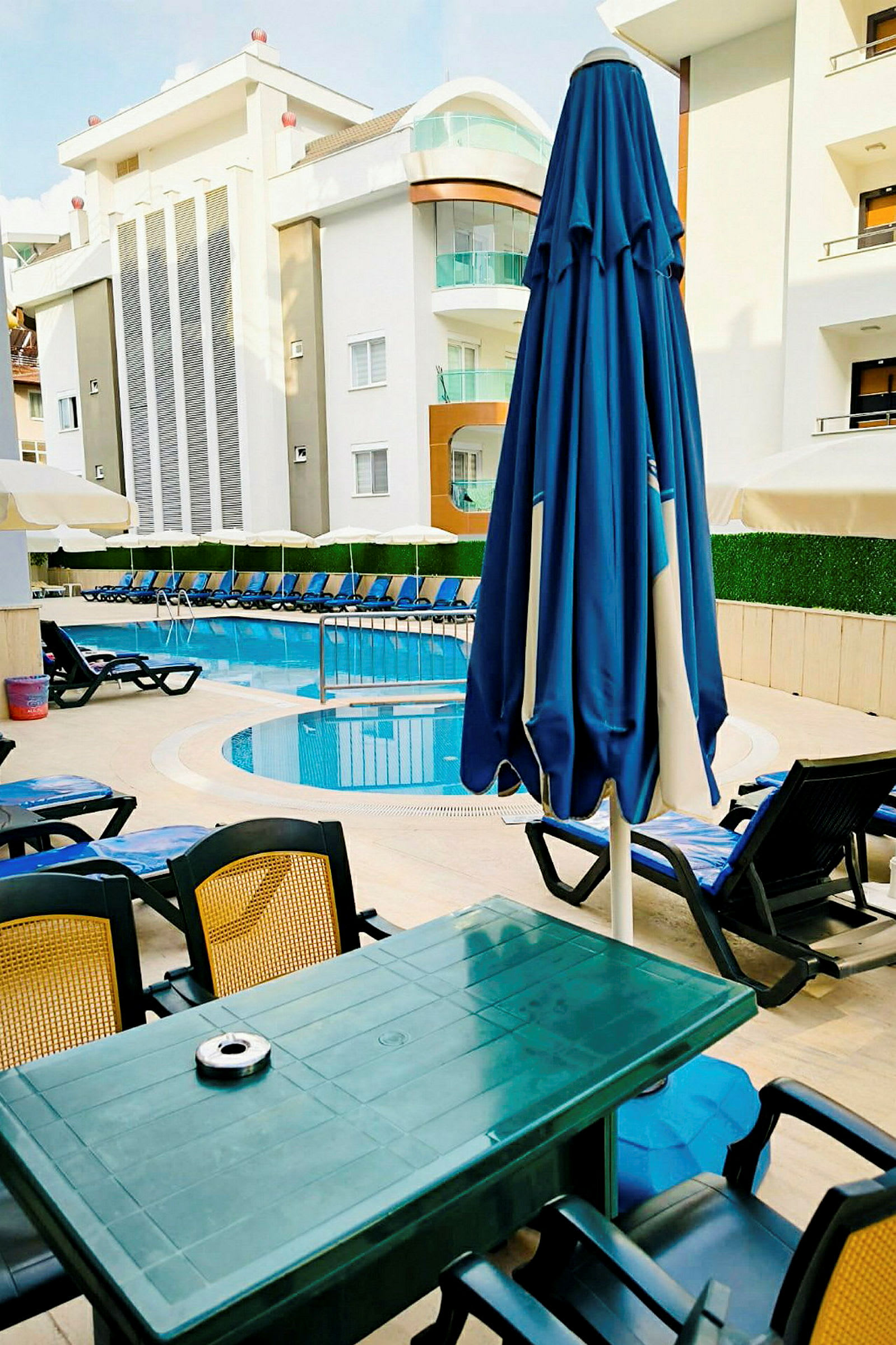 Liggestole og parasoller ved poolområdet foran et hotel. (AI-genereret tekst)