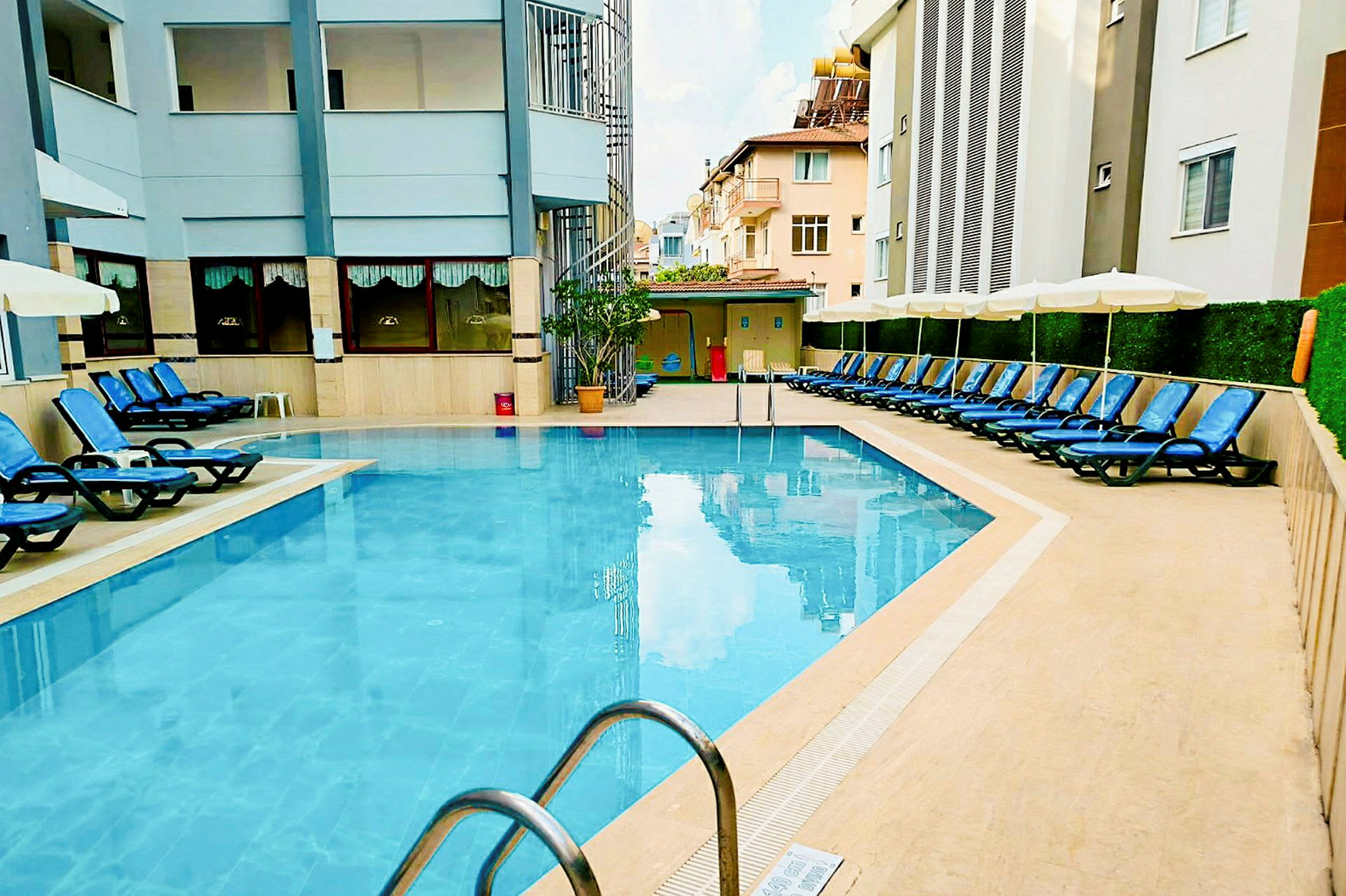 En udendørs pool omgivet af liggestole og bygninger. (AI-genereret tekst)