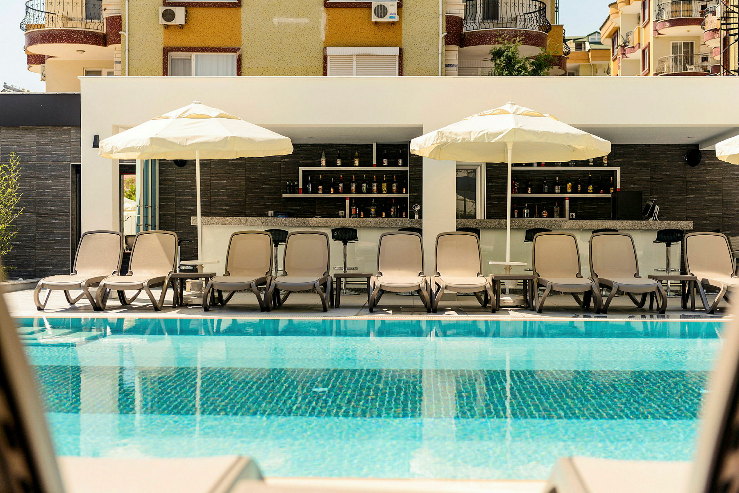 Liggestole og parasoller ved en pool med en bar i baggrunden. (AI-genereret tekst)