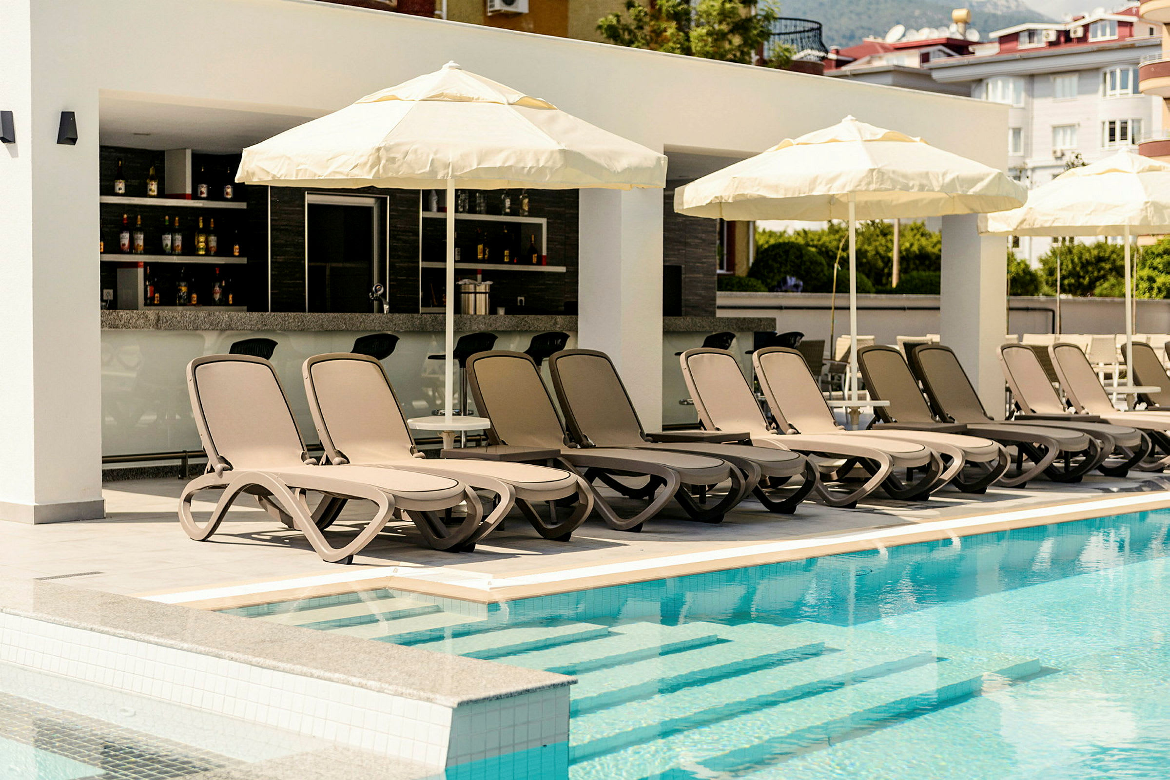 Liggestole og parasoller ved en swimmingpool med en bar i baggrunden. (AI-genereret tekst)