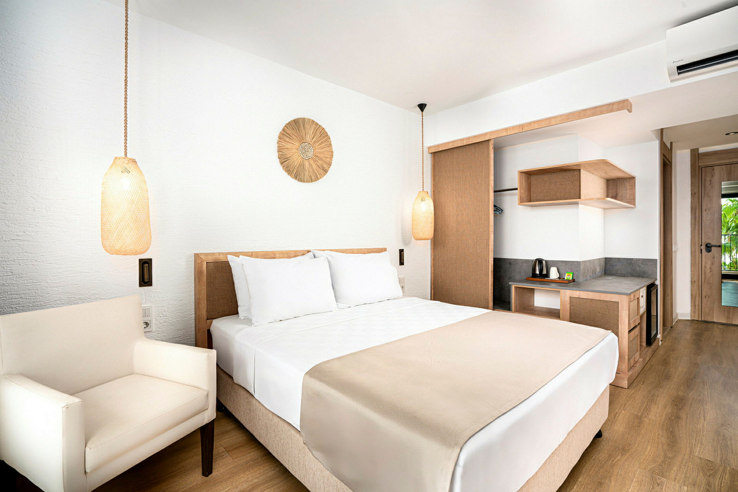Hotelværelse med en dobbeltseng, hvide sengelinned og beige detaljer. Rummet har en lænestol og en skriveplads med elkedel. (AI-genereret tekst)
