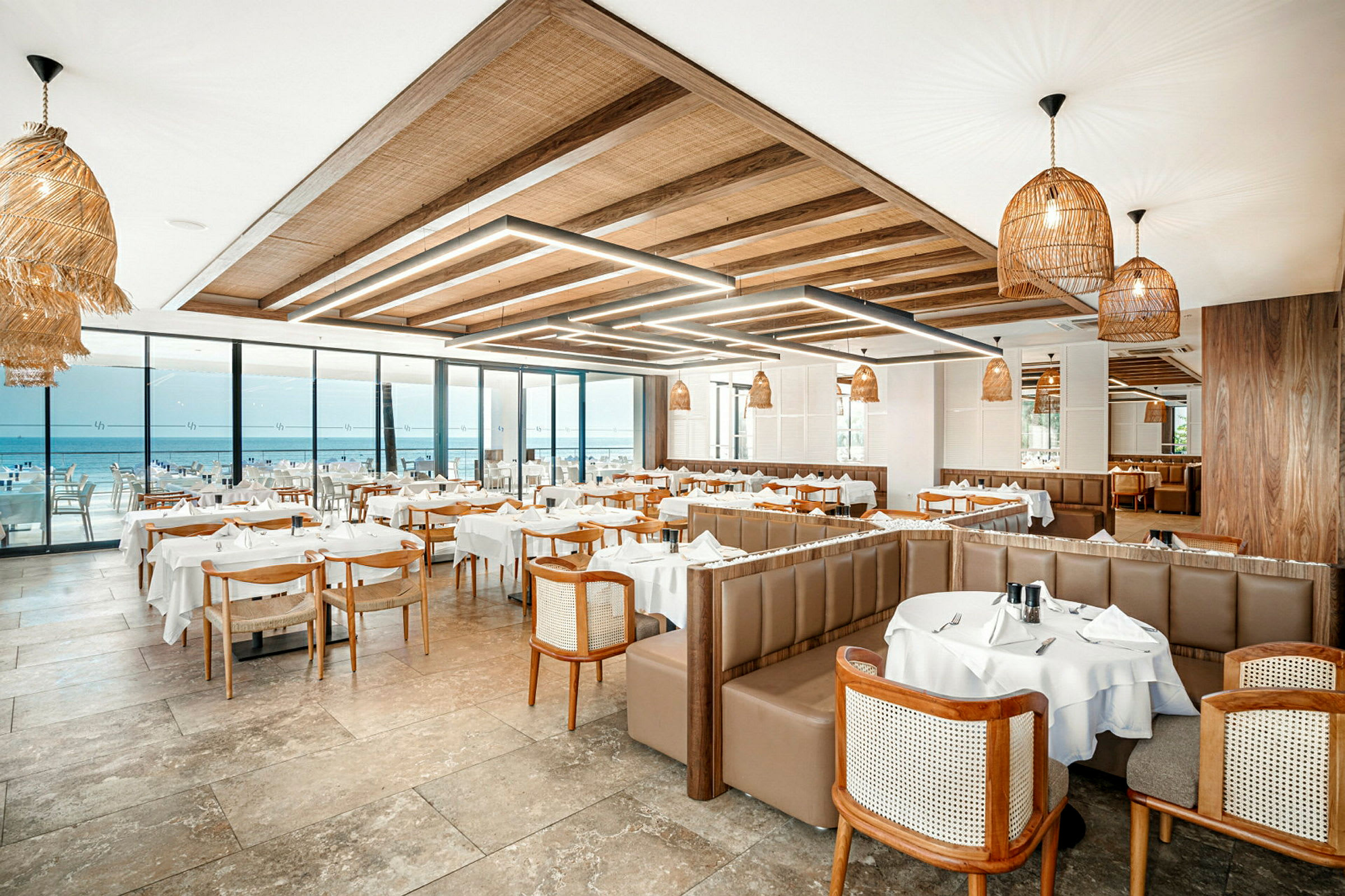 Restaurant med borde dækket med hvide duge og udsigt over havet. (AI-genereret tekst)