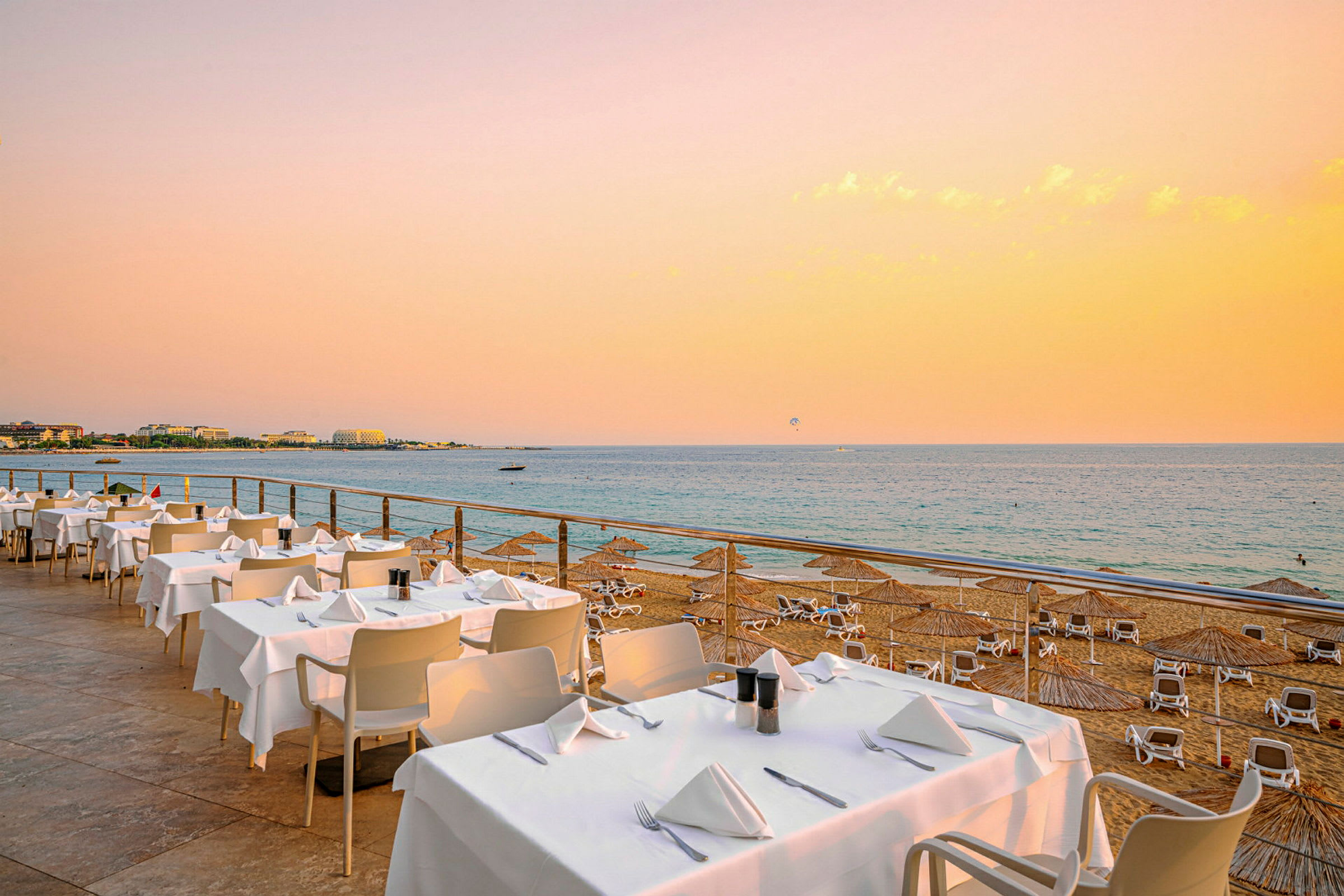 Billede af en strand med liggestole og parasoller samt en restaurant med opkladte borde ved havet. (AI-genereret tekst)