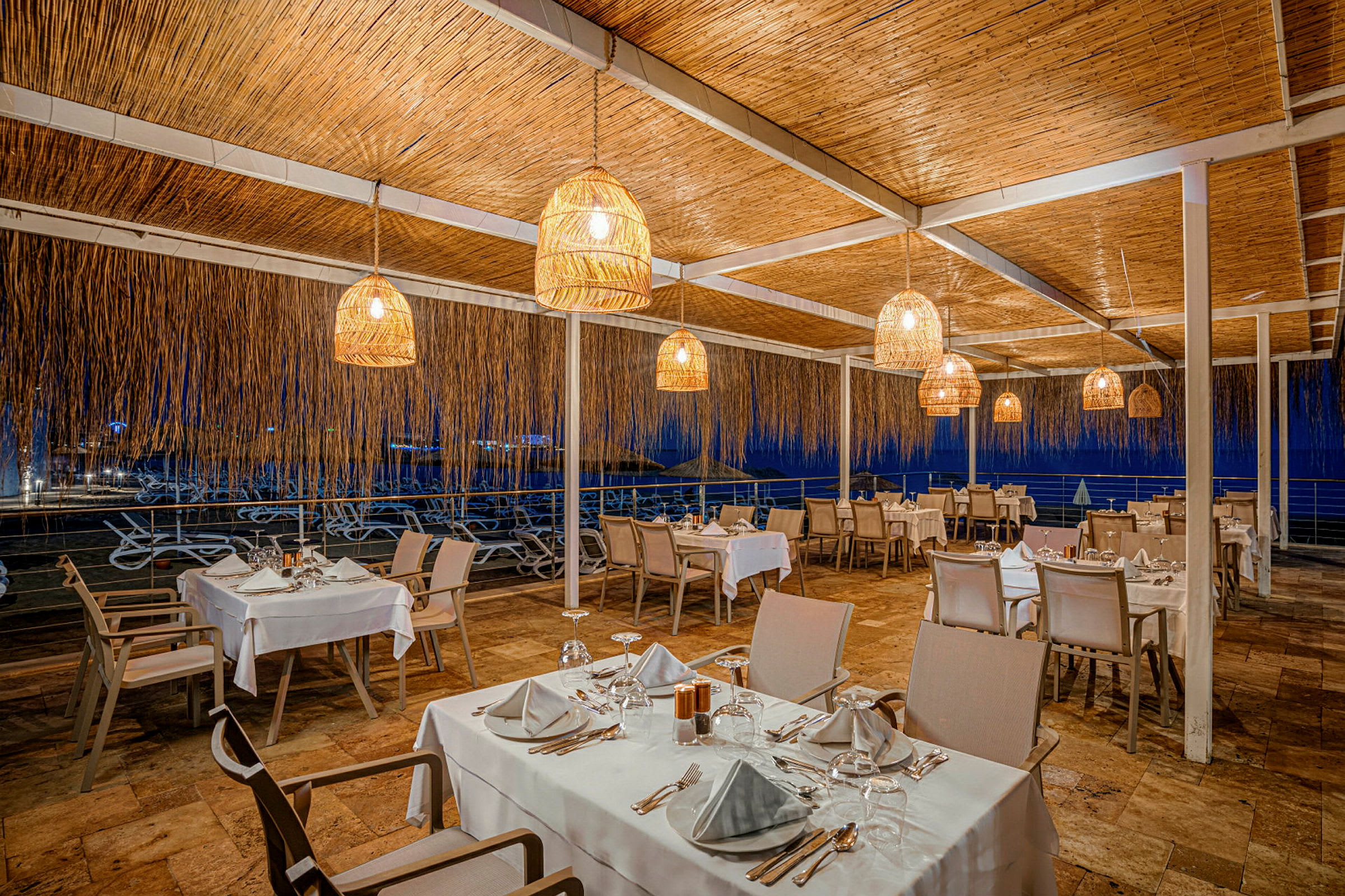 En udendørs restaurant med opfyldte borde, oplyst af hængende lamper. (AI-genereret tekst)