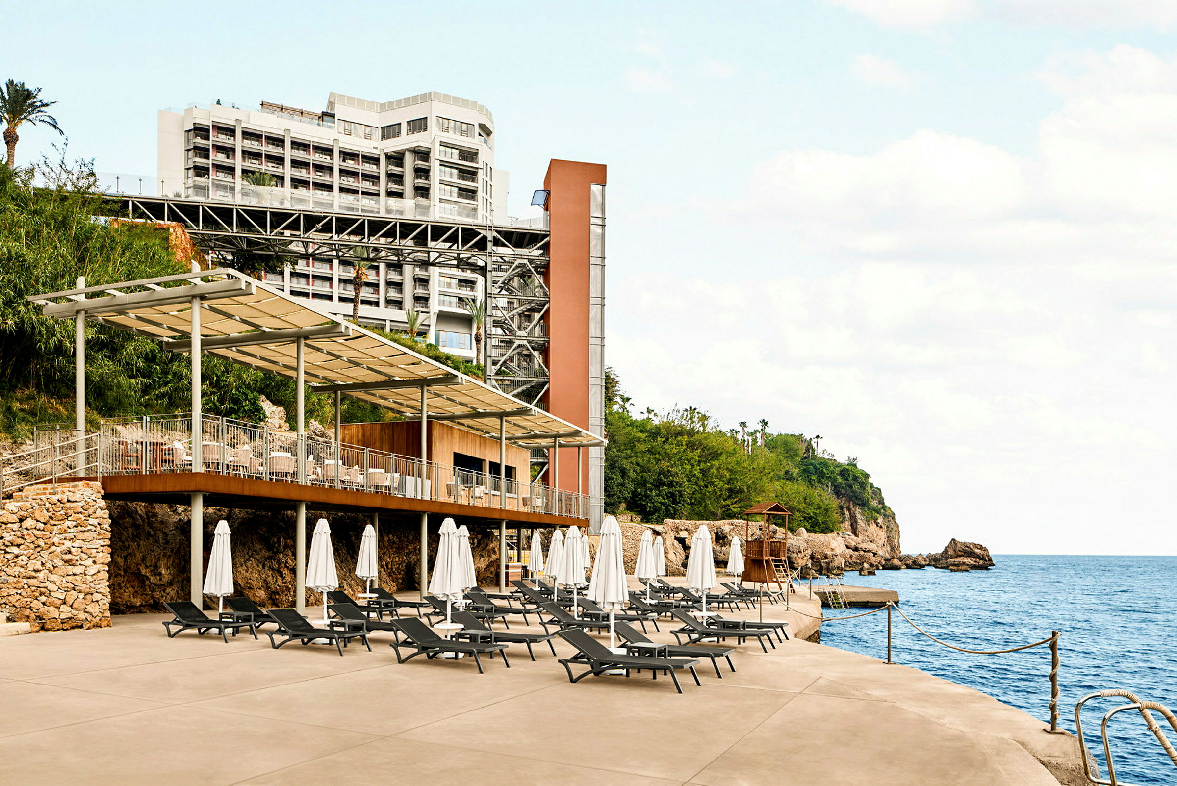 Hotel med terrasse og solvogne ved havet. (AI-genereret tekst)
