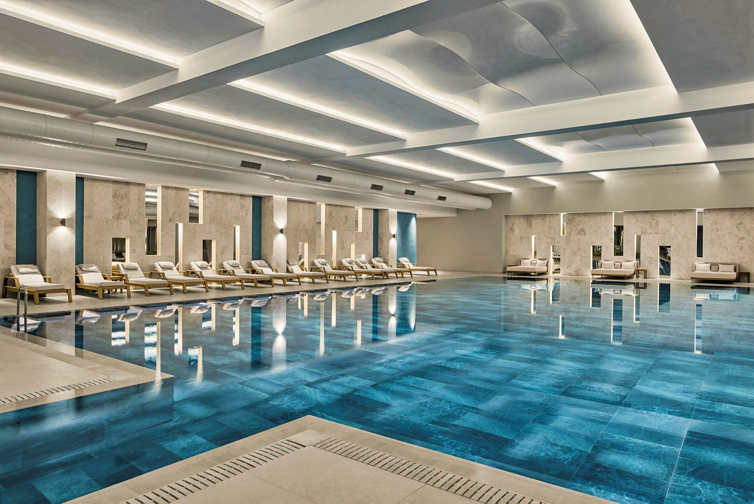En indendørs pool omgivet af liggestole og siddeområder med moderne design. (AI-genereret tekst)