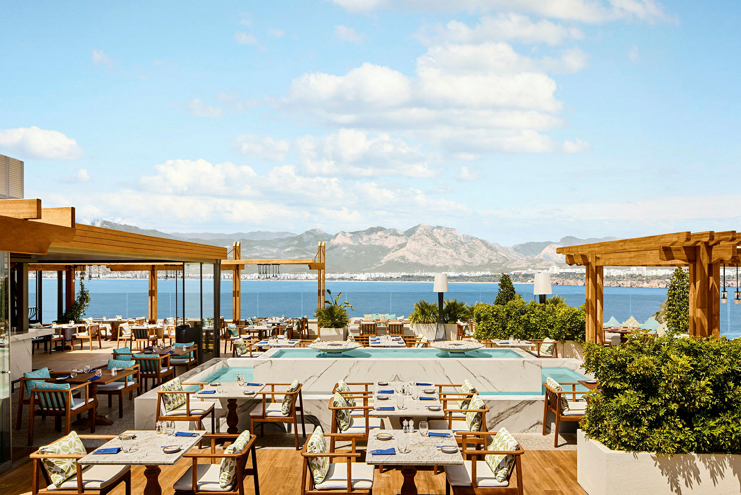 En restaurantterrasse med havudsigt og bjerge i baggrunden. (AI-genereret tekst)