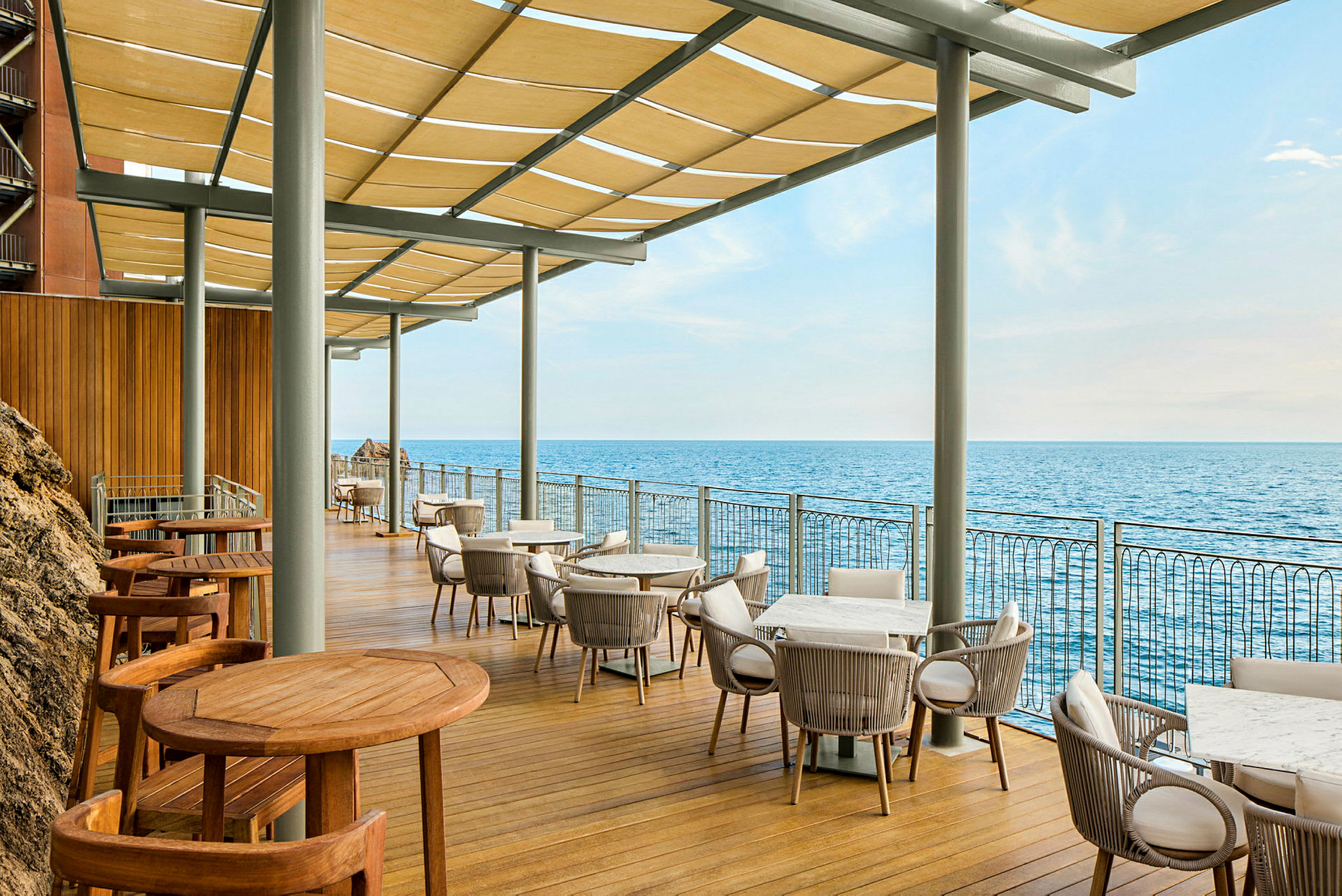 En terrasse med borde og stole med udsigt over havet. (AI-genereret tekst)