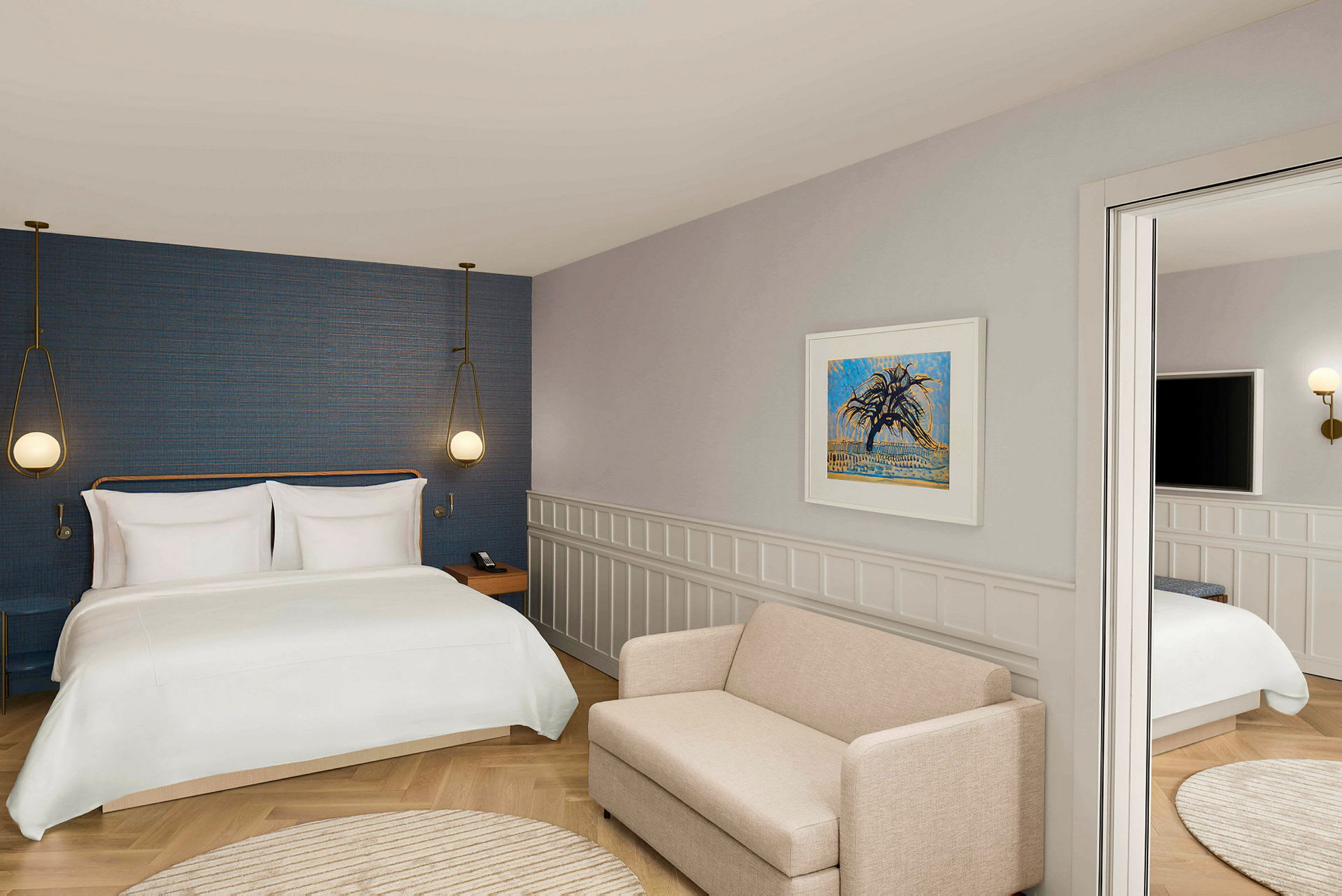 Et hotelværelse med en stor seng, væglamper, en beige sofa og kunst på væggen. (AI-genereret tekst)