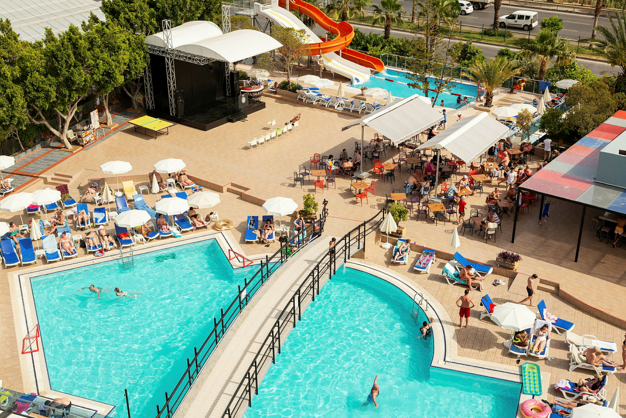 Udsigt over hotelområde med pools, liggestole og vandrutsjebane. (AI-genereret tekst)