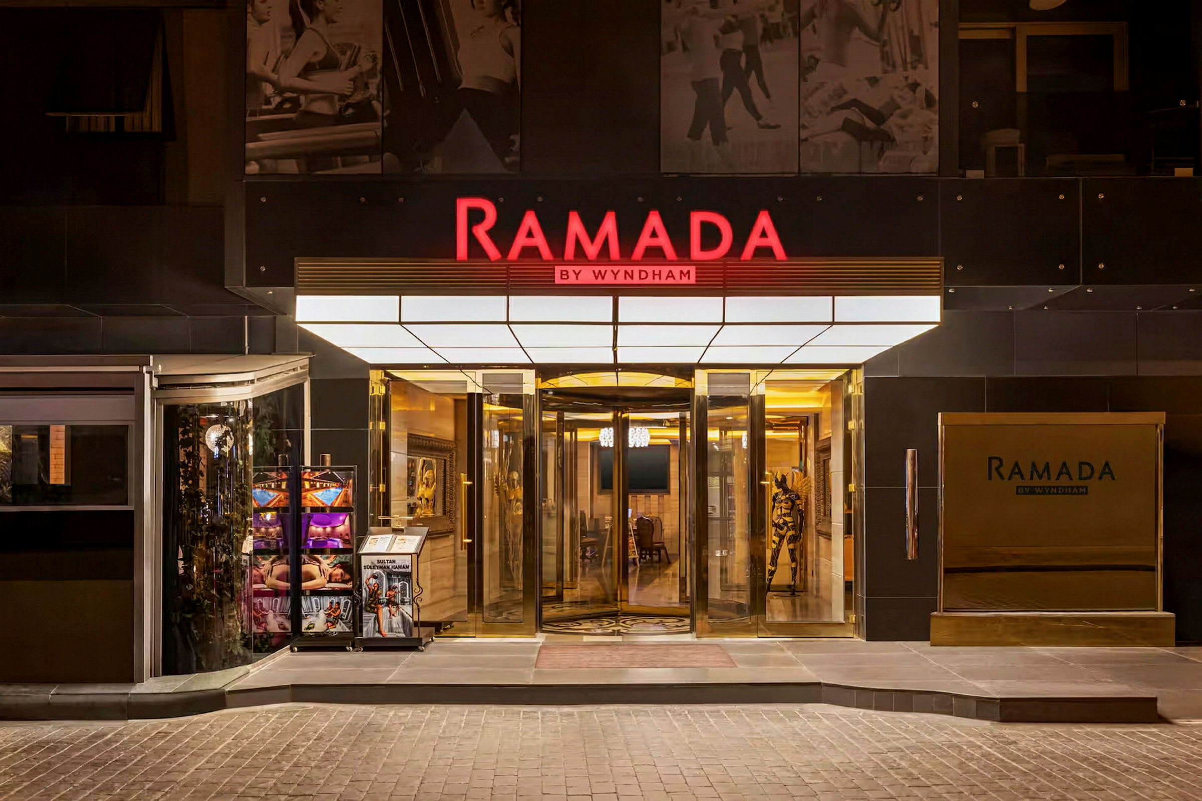 Hovedindgangen til hotelkæden Ramada by Wyndham, med en drejedør og skilte. (AI-genereret tekst)