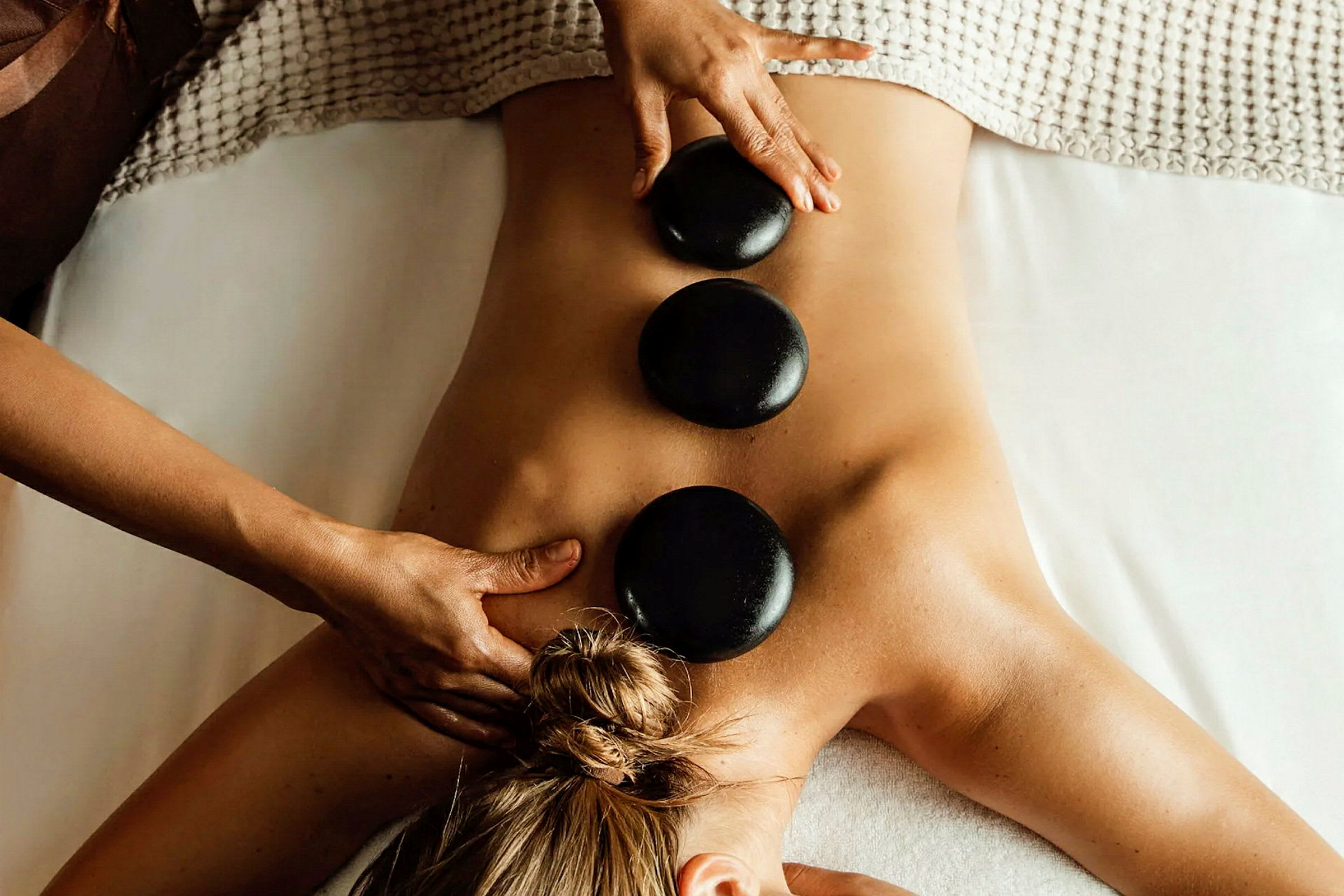 En person får rygmassage med varme sten placeret på ryggen. (AI-genereret tekst)