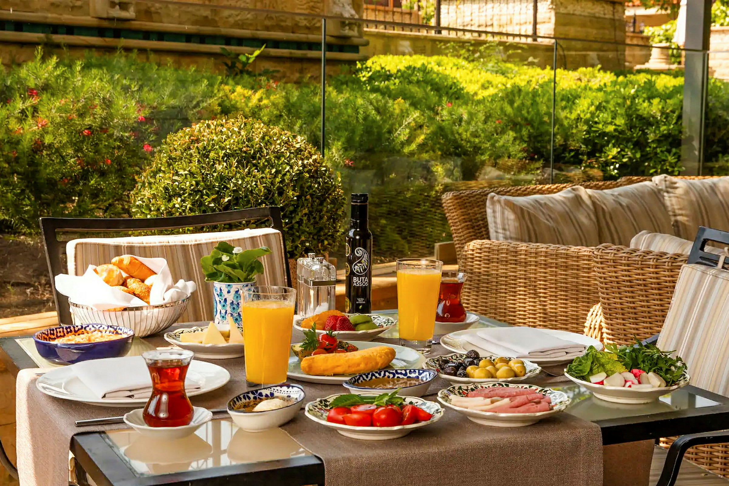 Et farverigt morgenbord med forskellige retter, juice og te, placeret udendørs med grønne omgivelser i baggrunden. (AI-genereret tekst)