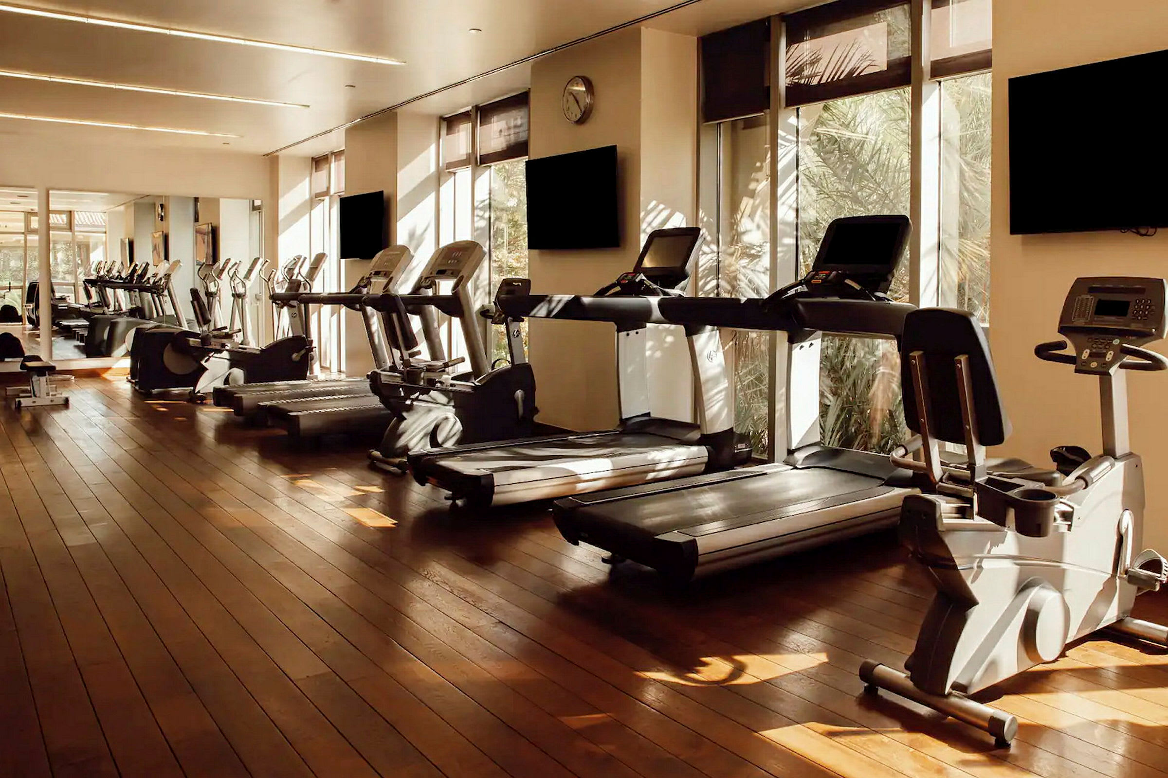 Et fitnesscenter med løbebånd, træningsmaskiner og motionscykler i et solbelyst rum. (AI-genereret tekst)