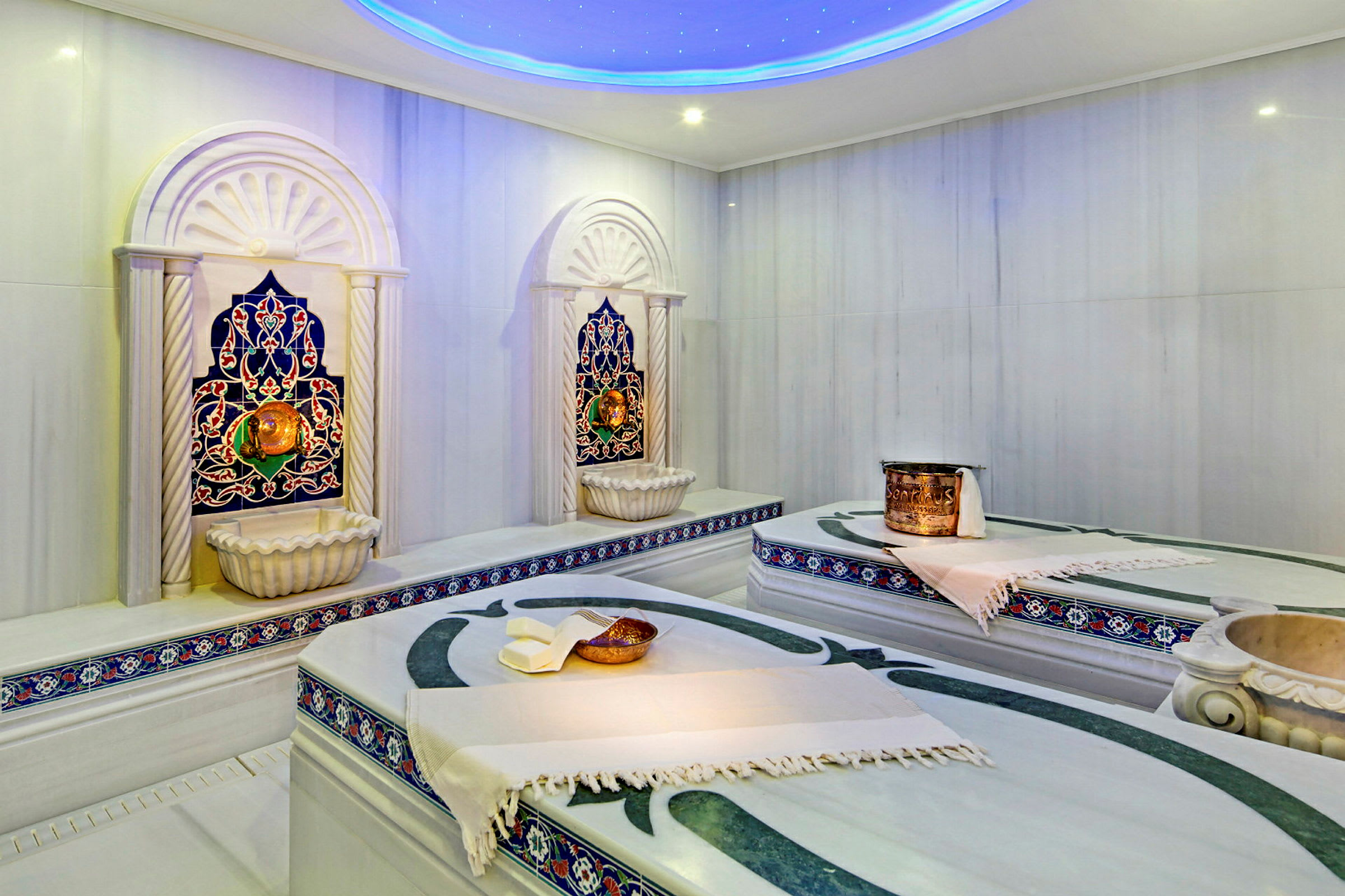 Et traditionelt hamam med marmorbænke, dekorative springvand og farverige mosaikdetaljer. (AI-genereret tekst)