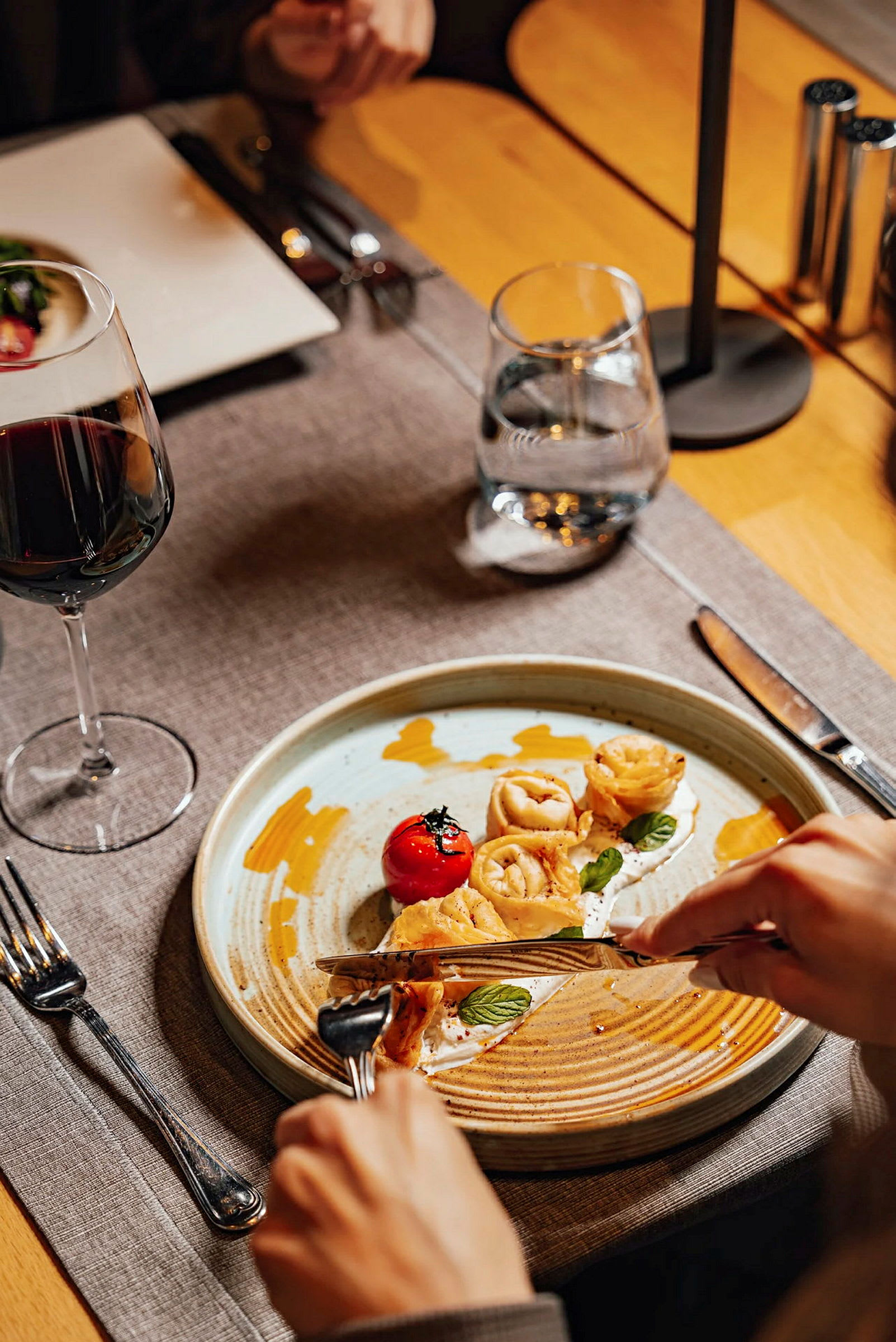 En tallerken med mad, omkranset af bestik, et glas vand og et glas vin. (AI-genereret tekst)