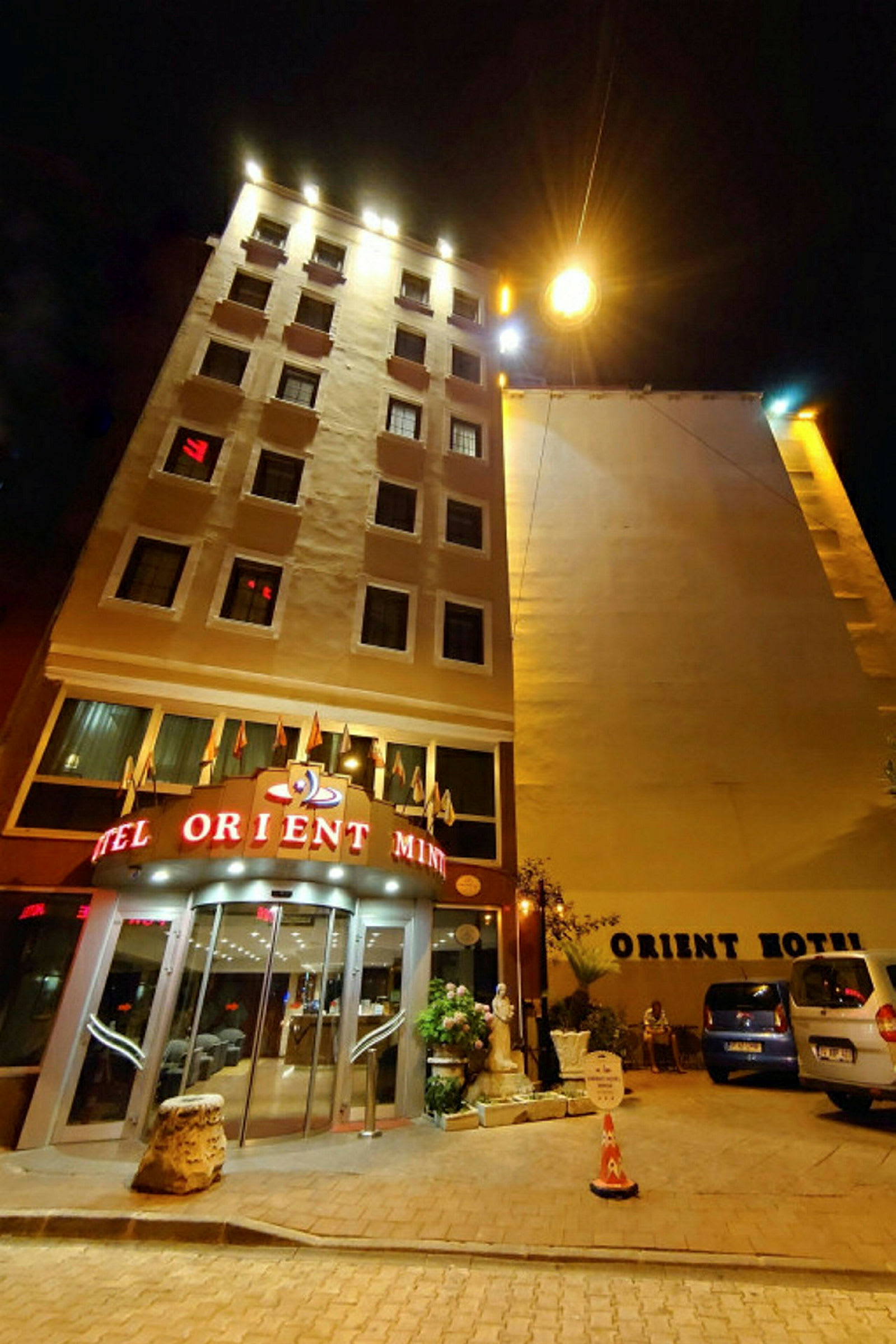 Et hotel om natten, med skilt og belysning på facaden samt parkerede biler udenfor. (AI-genereret tekst)