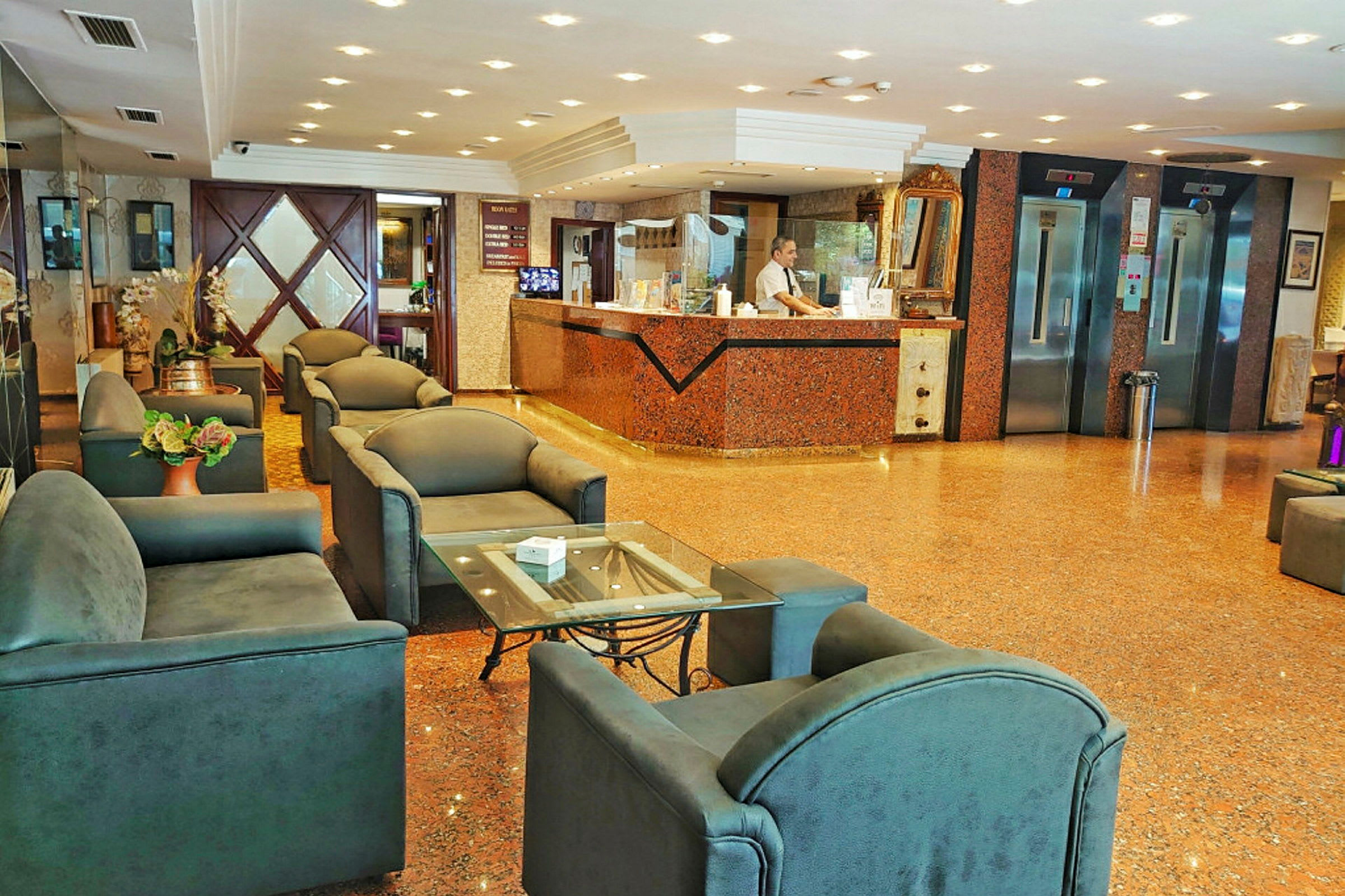 Billede af et hotel-lobbyområde med en receptionsdisk, siddegrupper og elevatorer. (AI-genereret tekst)