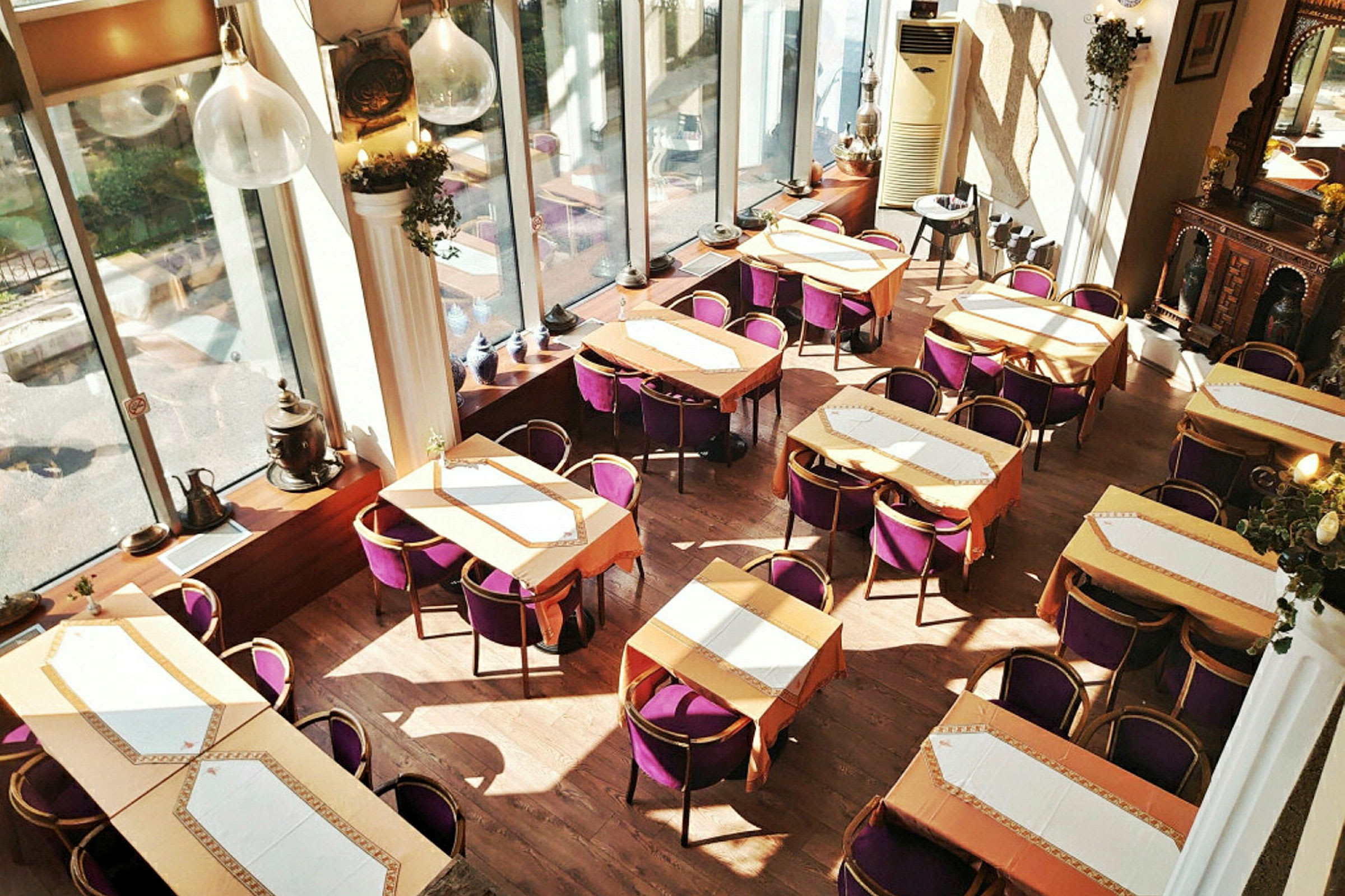 Interiør af en restaurant med flere borde og lilla stole, store vinduer og dekorative elementer. (AI-genereret tekst)
