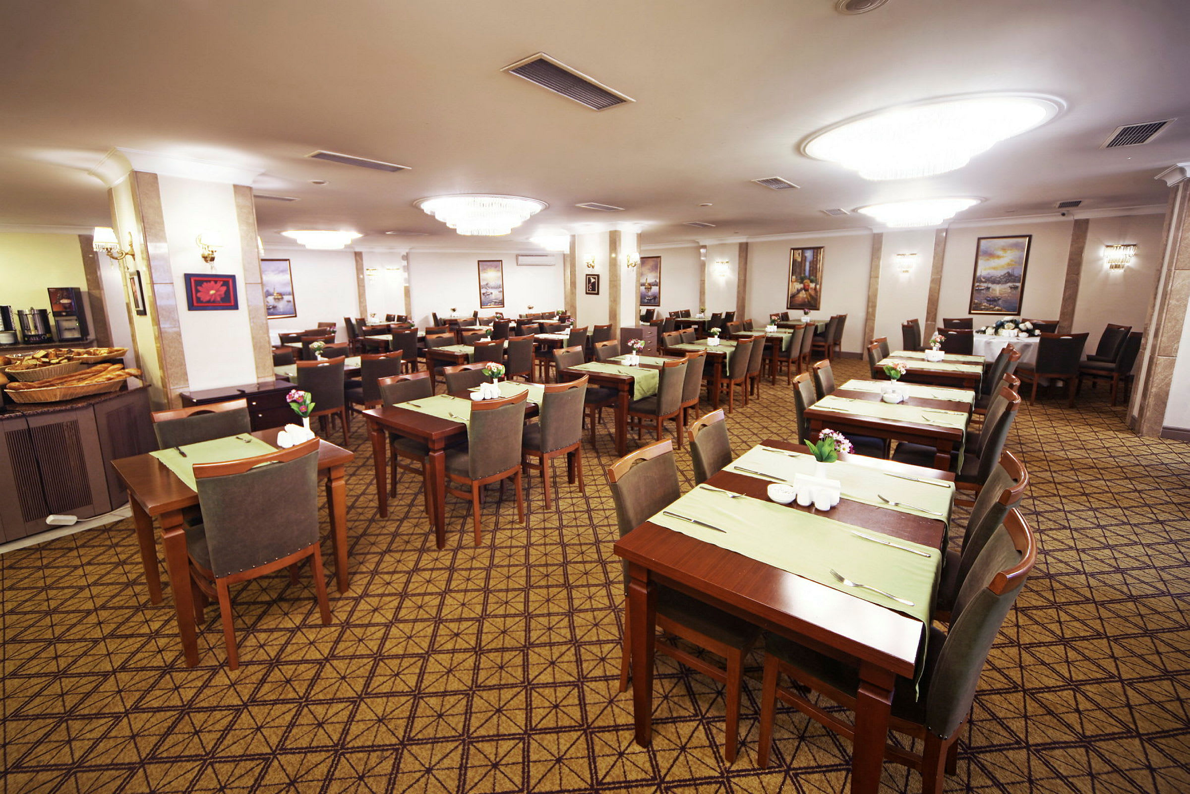 Restaurant med flere opstillede borde og stole, dækket med grønne underlag og blomsterdekorationer. (AI-genereret tekst)