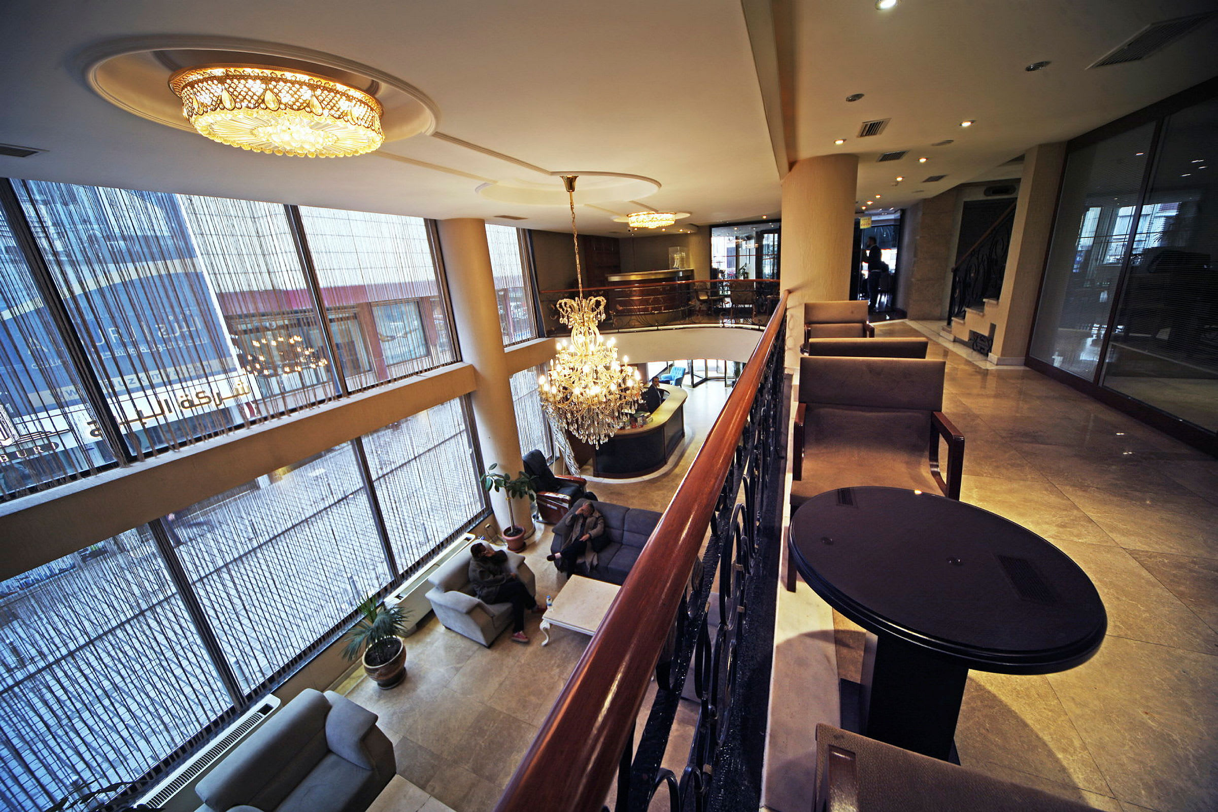 Billede af en hotellobby med store glasvinduer, loftlamper og en lysekrone. Møblerede siddepladser findes på forskellige niveauer. (AI-genereret tekst)