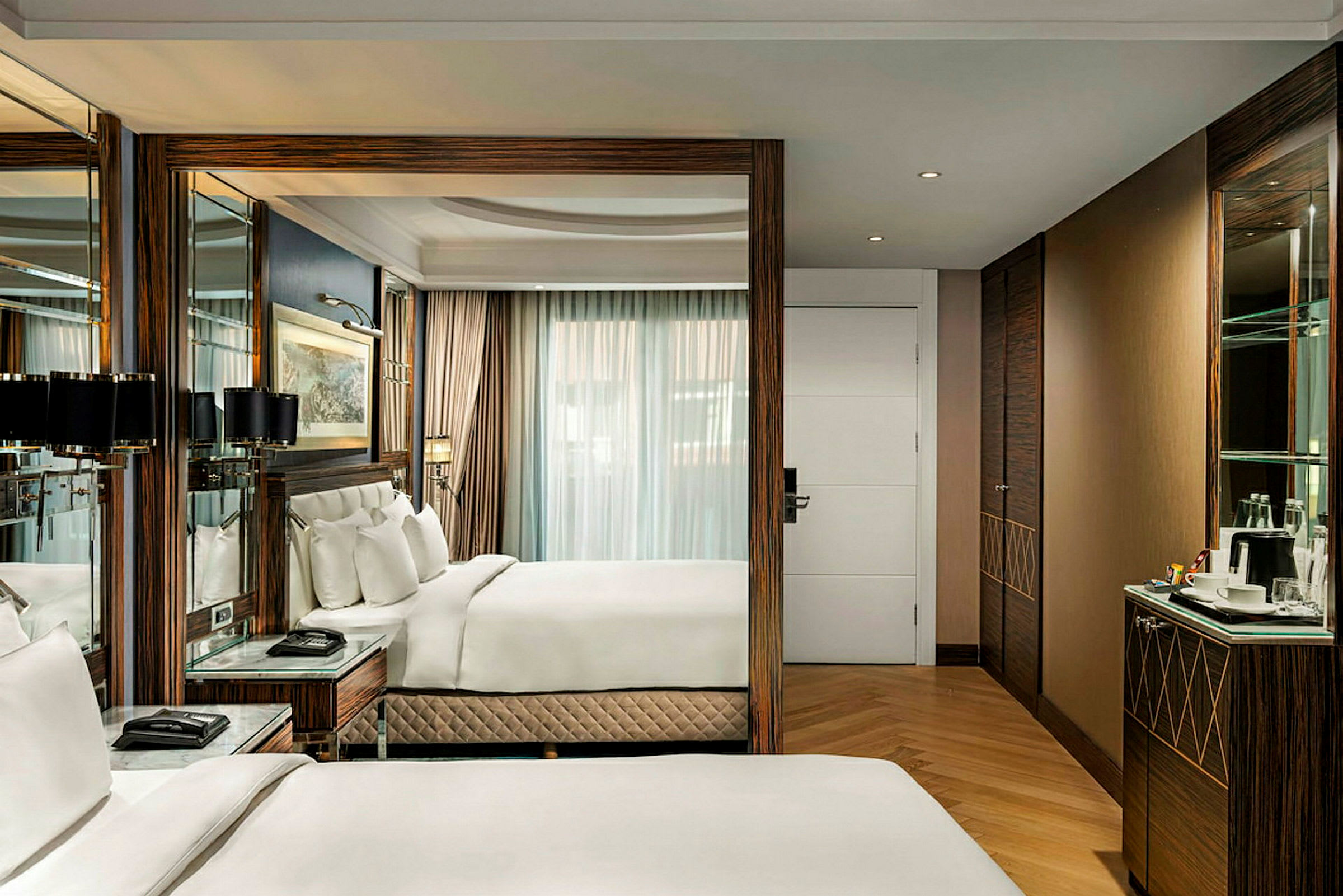 Et elegant og moderne hotelværelse med komfortable senge og interiør i træ, en spejlvæg og store vinduer med gardiner. (AI-genereret tekst)