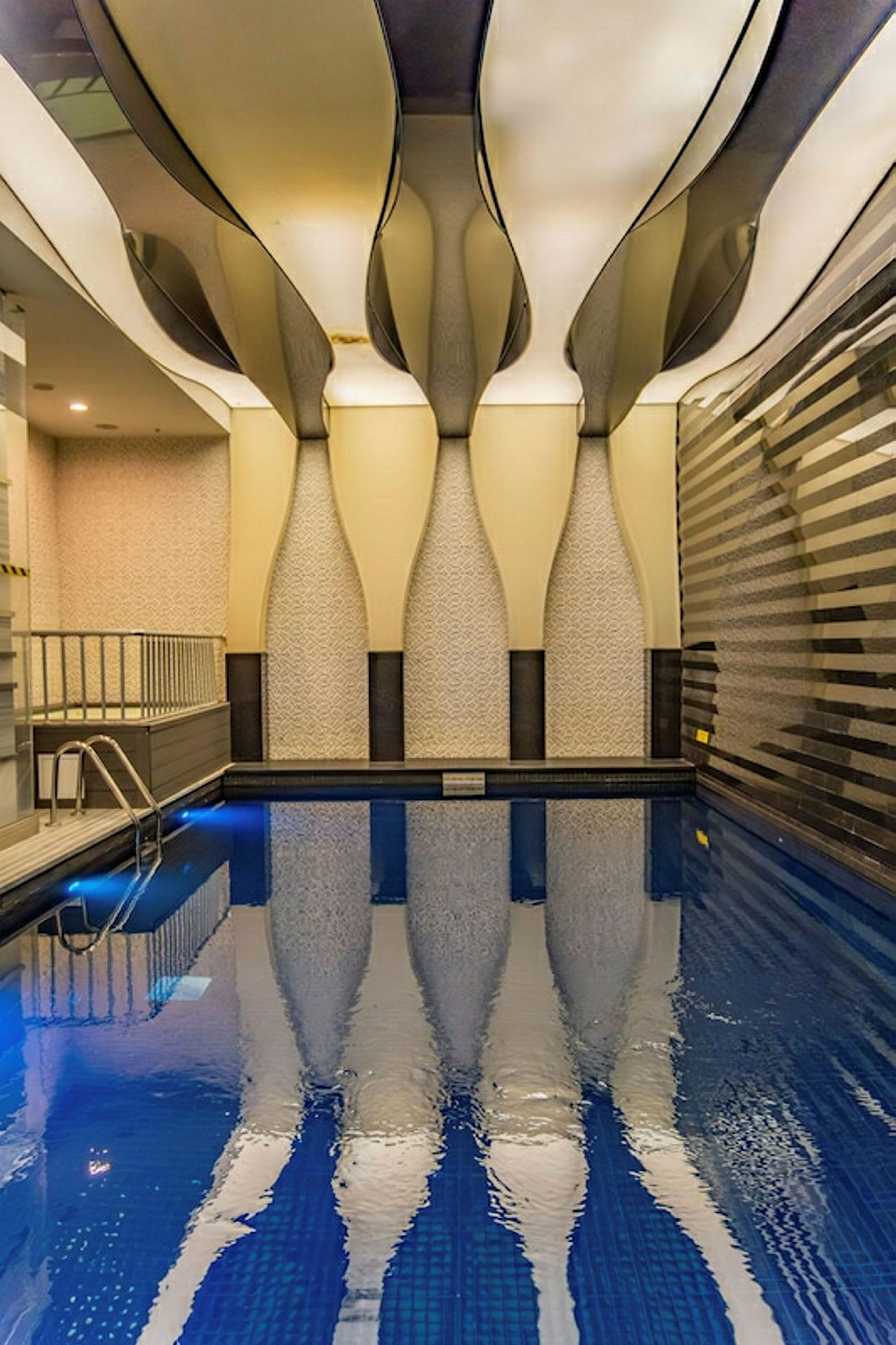 En indendørs pool med unikt designet loft og mønstrede vægge. Vandet spejler arkitekturen ovenfor. (AI-genereret tekst)