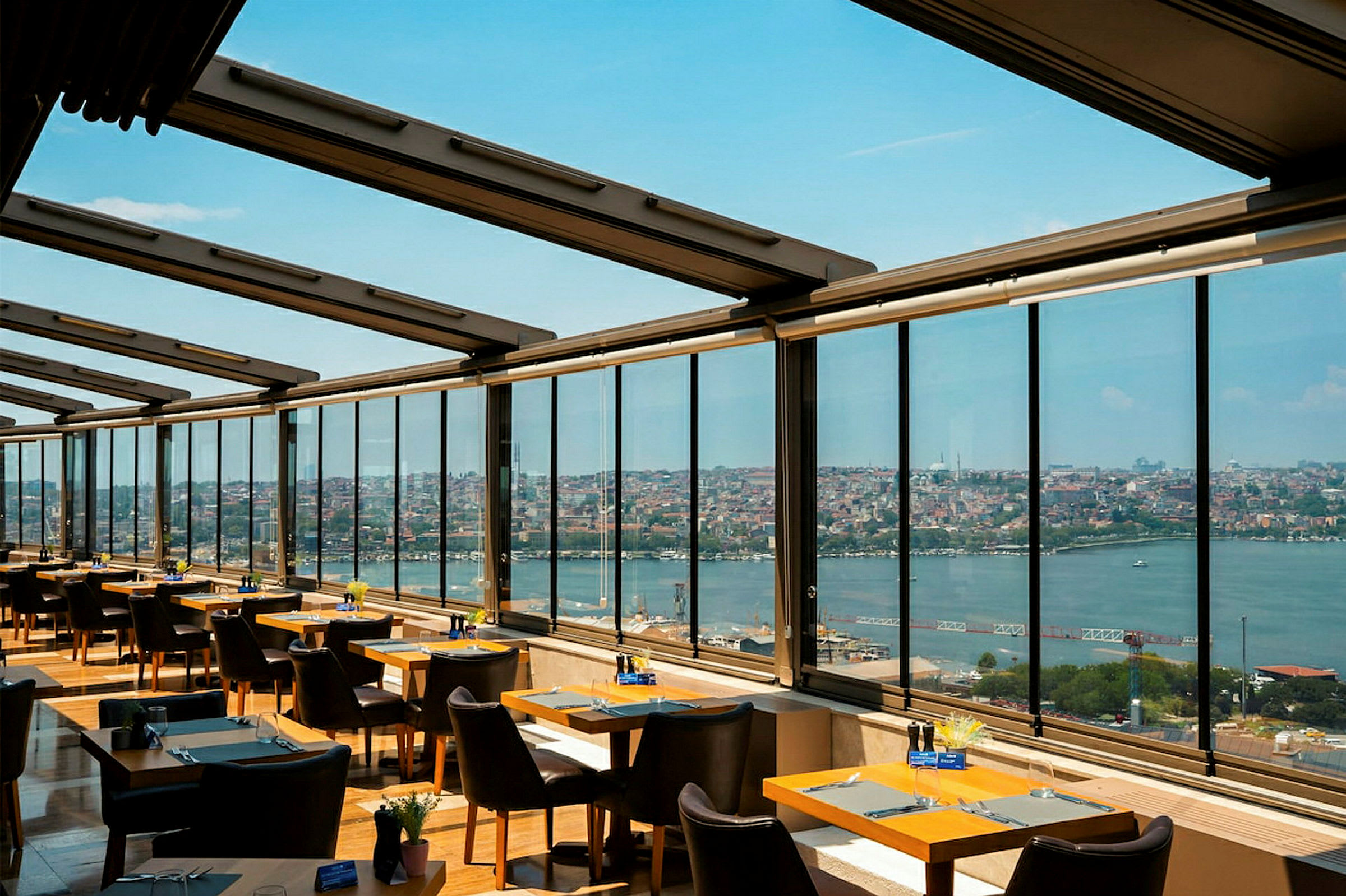 En restaurant med store vinduer, der giver udsigt til en by og et vandløb. (AI-genereret tekst)