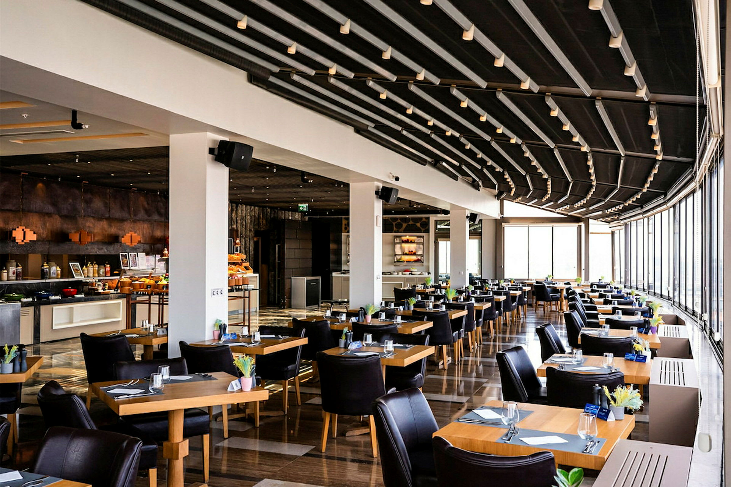 Restaurant med moderne indrettede borde og stole, stor glasflade, der lader lys komme ind. (AI-genereret tekst)