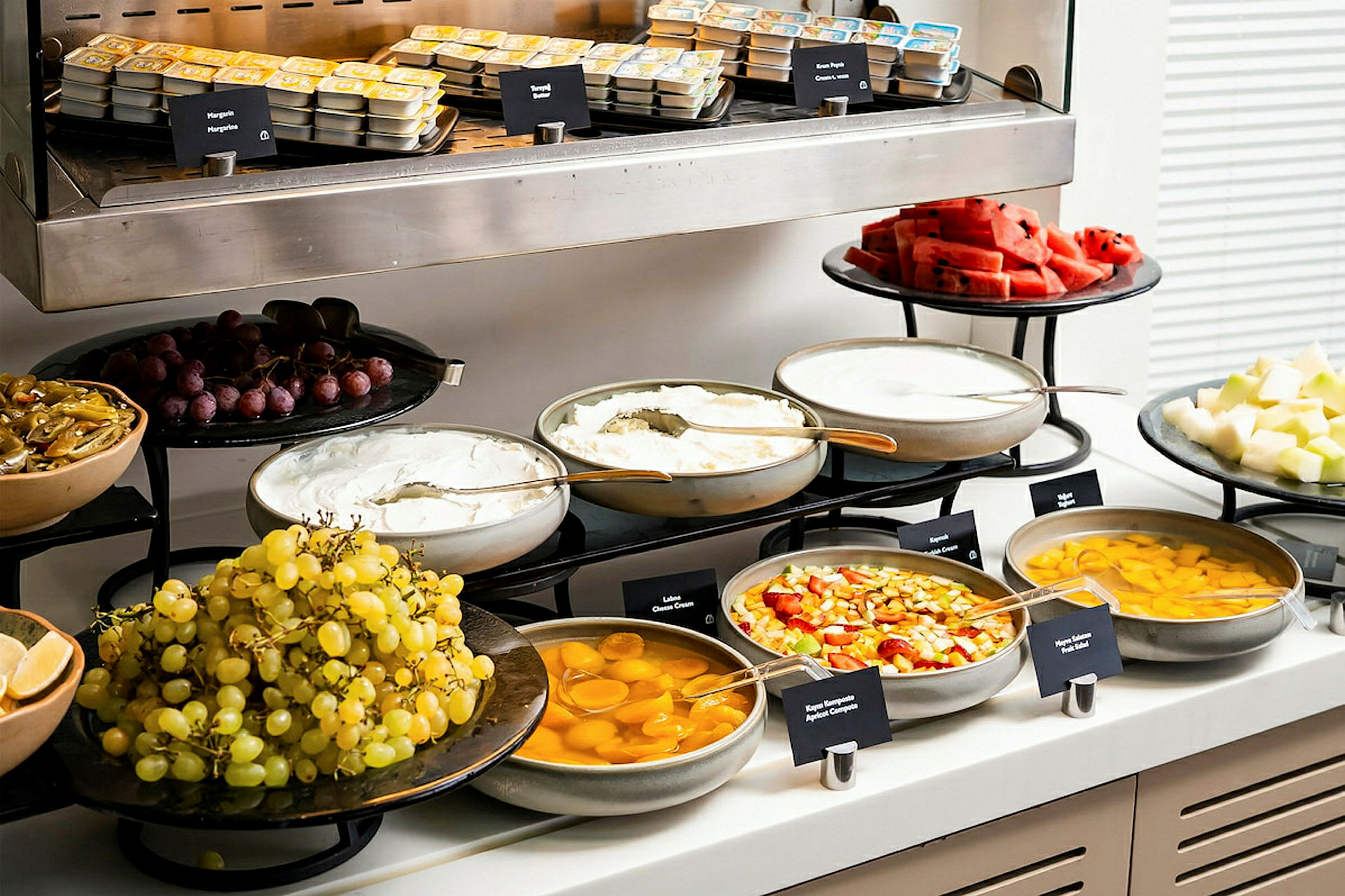 En buffet med et udvalg af frugt, yoghurt, dåsefrugt og smørpakker. (AI-genereret tekst)