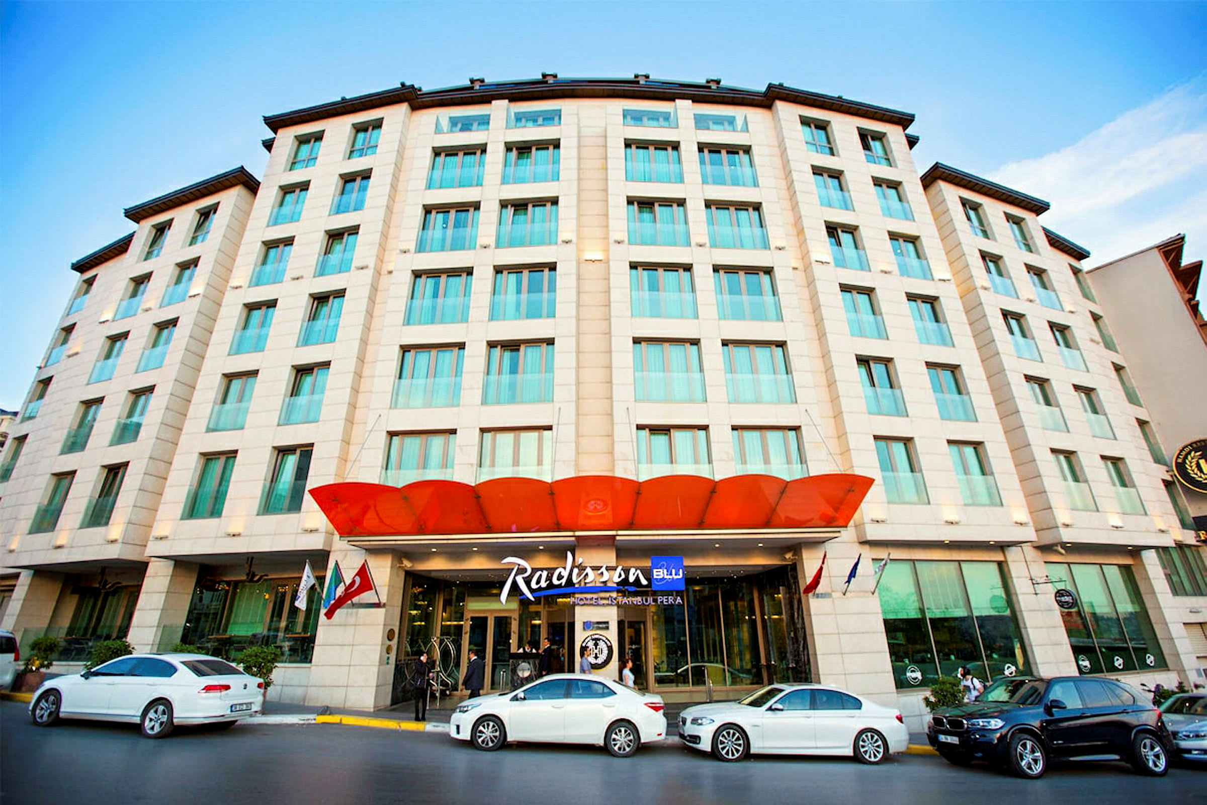 Et fleretagers hotelbygning med en orange baldakin ved indgangen og navnet Radisson tydeligt synligt. (AI-genereret tekst)