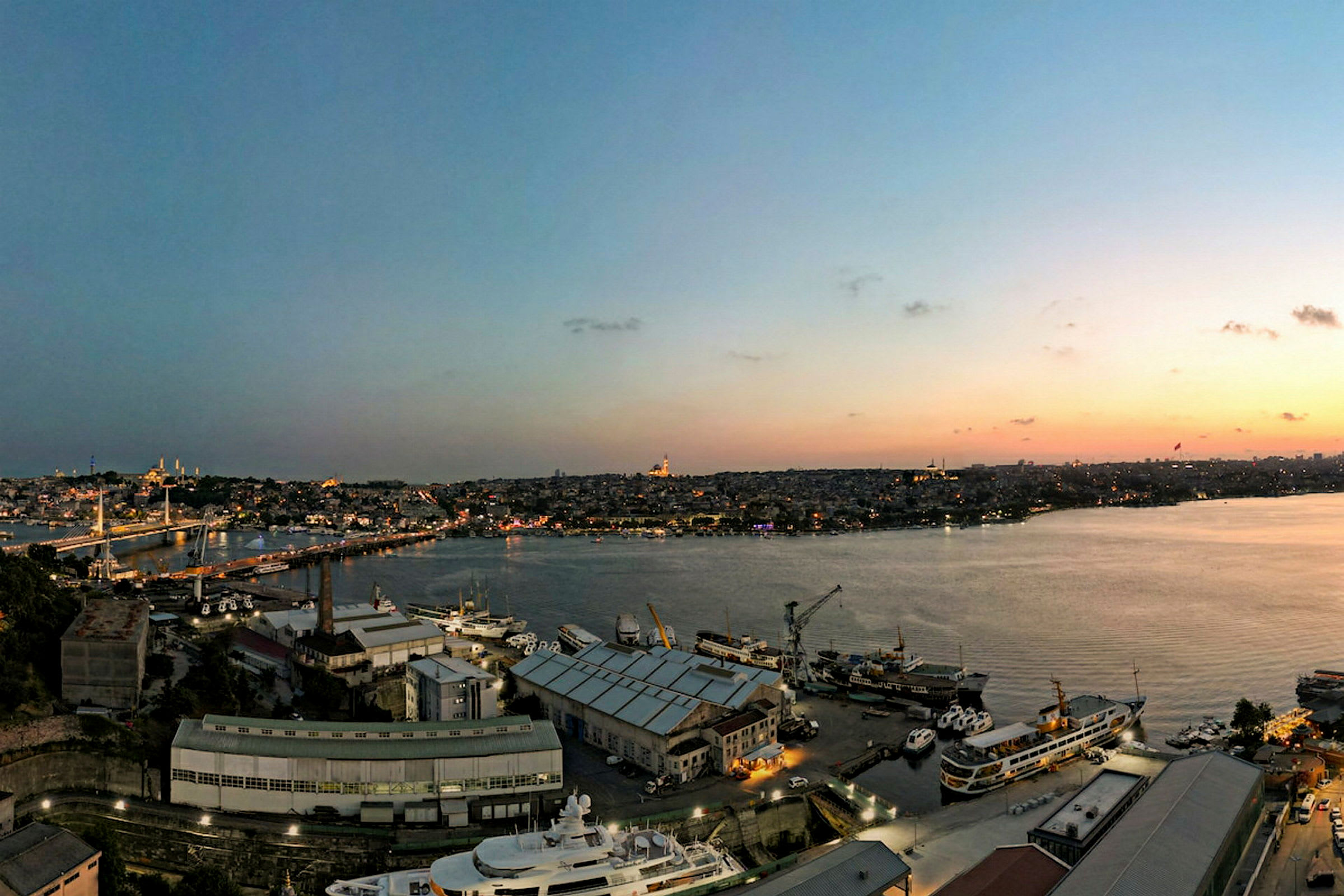 Udsigt over en havn med både og by i baggrunden under solnedgang. (AI-genereret tekst)