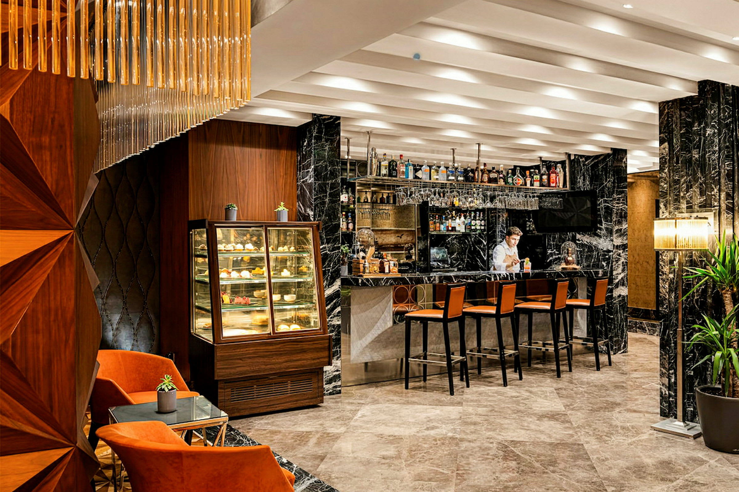 Interiør af en elegant bar med marmordetaljer, en samling af alkoholiske drikkevarer på hylderne, stole ved baren og en display for bagværk. (AI-genereret tekst)